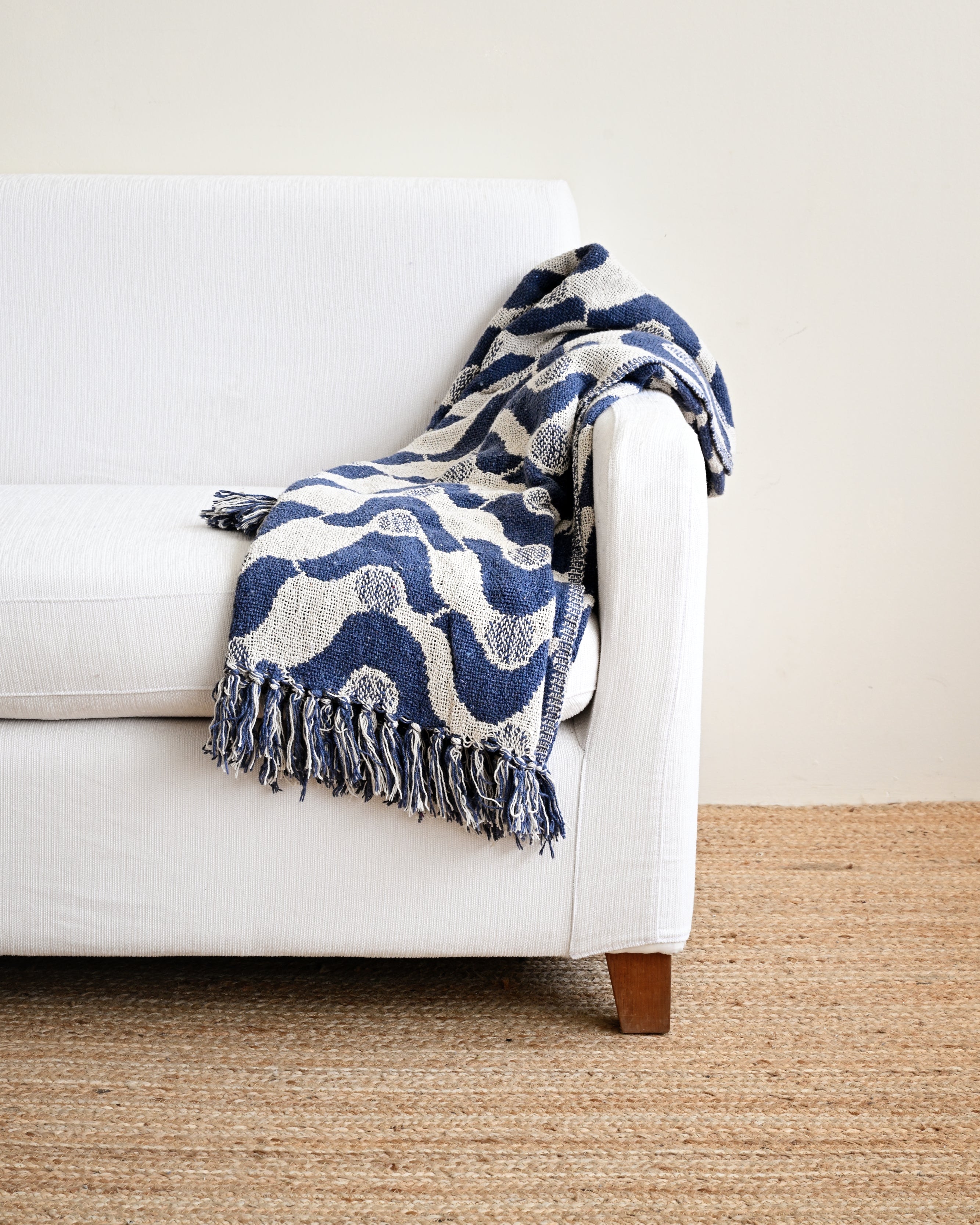 White sofa with a blue and white patterned throw blanket on a beige carpet.