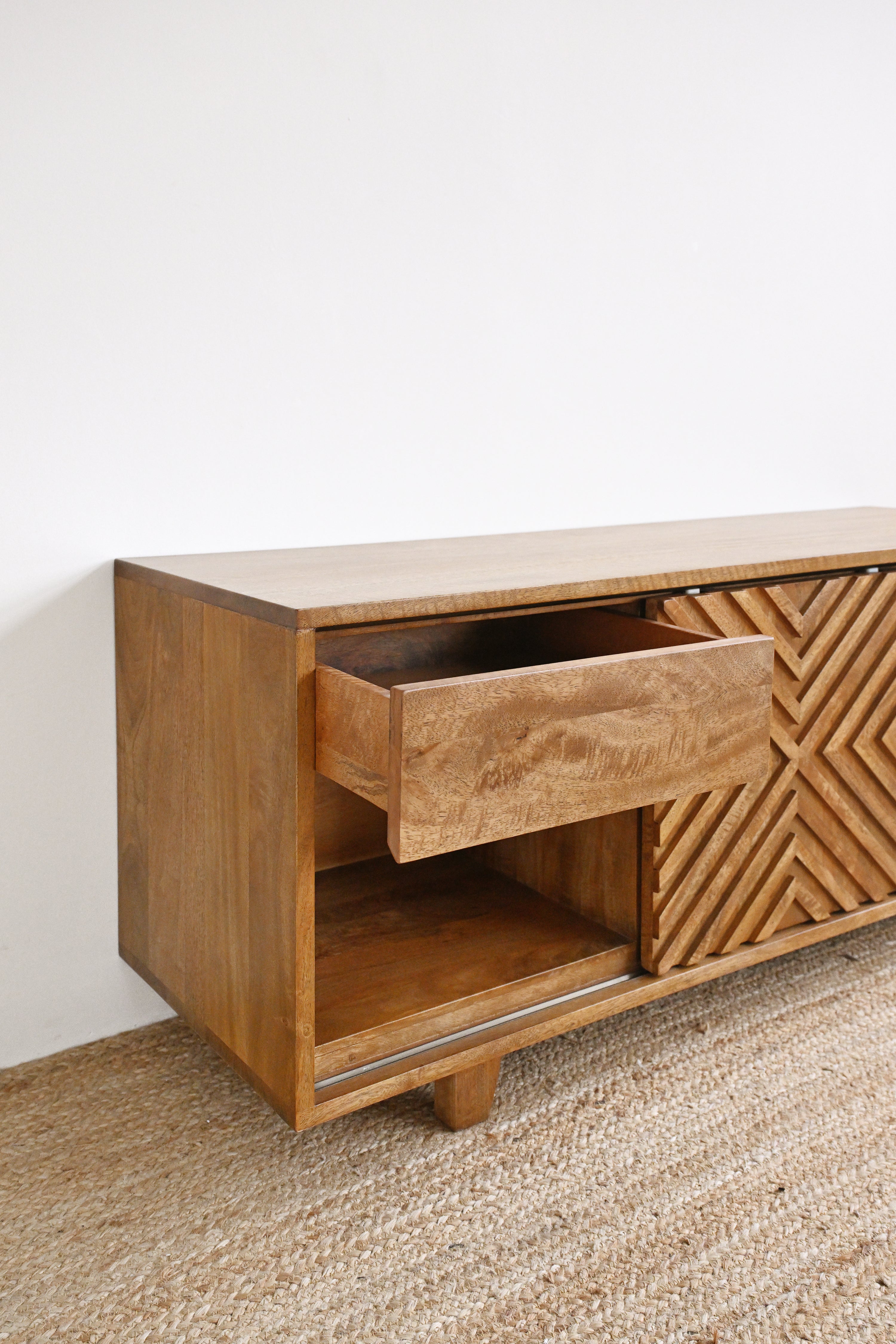 Wooden sideboard with a textured drawer and geometric pattern on a white wall background