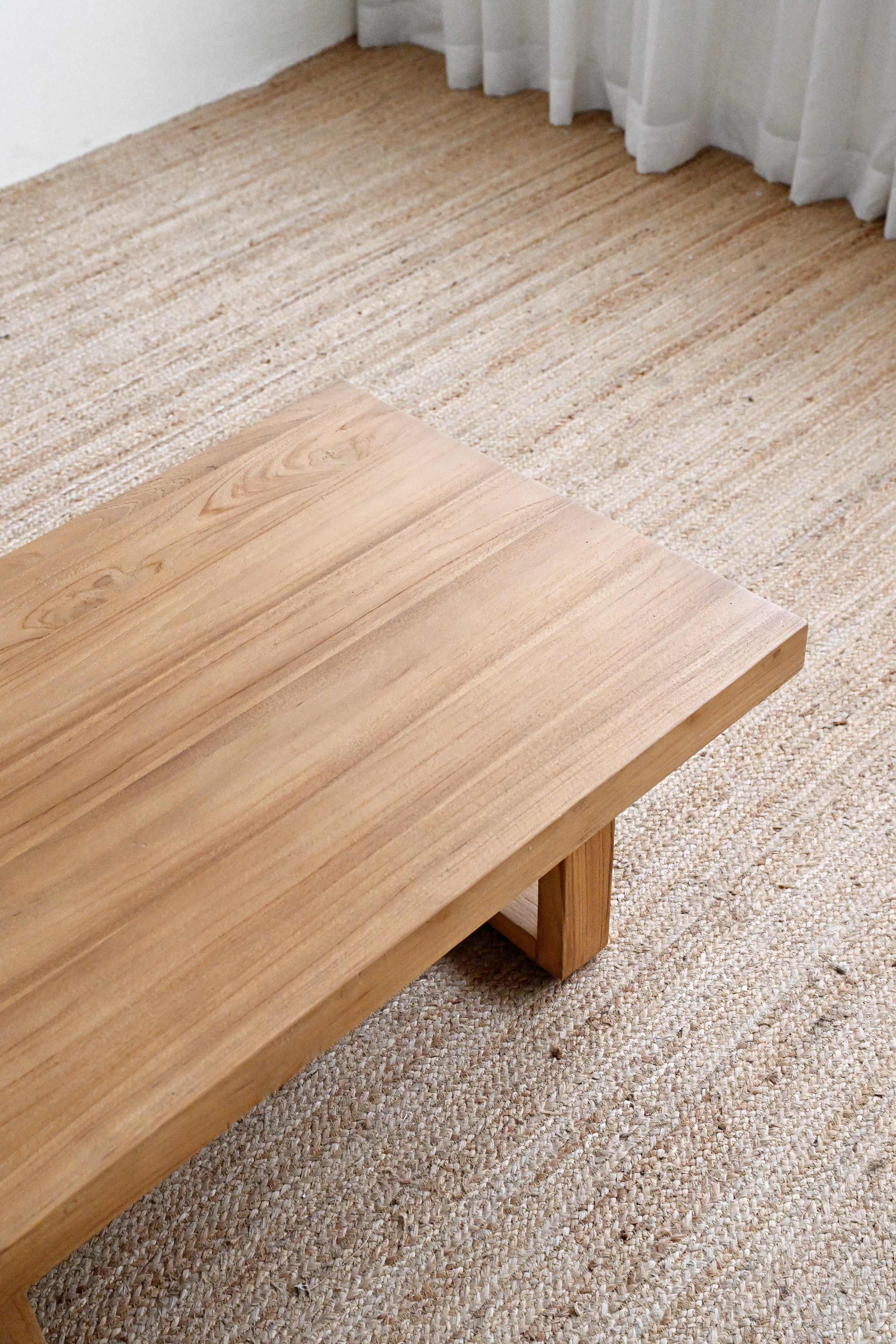 Wooden coffee table on a carpeted floor with a curtain in the background