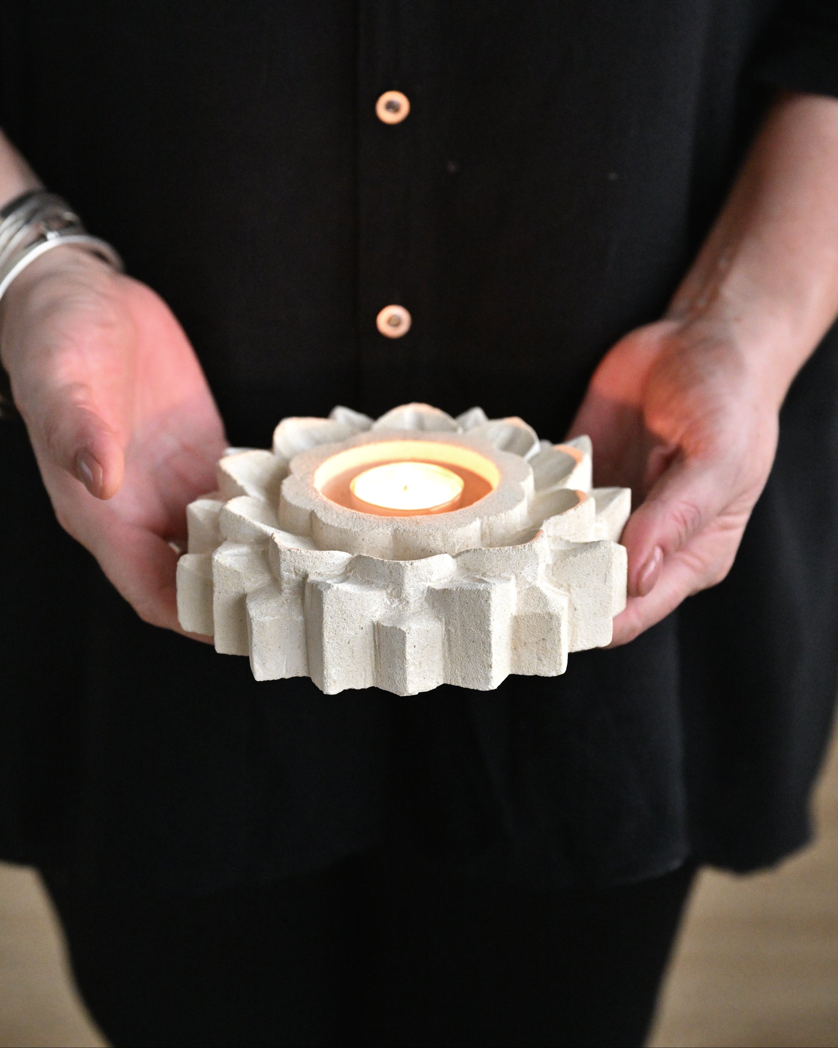 Person holding a white ceramic gear-shaped candle holder with a lit candle inside.