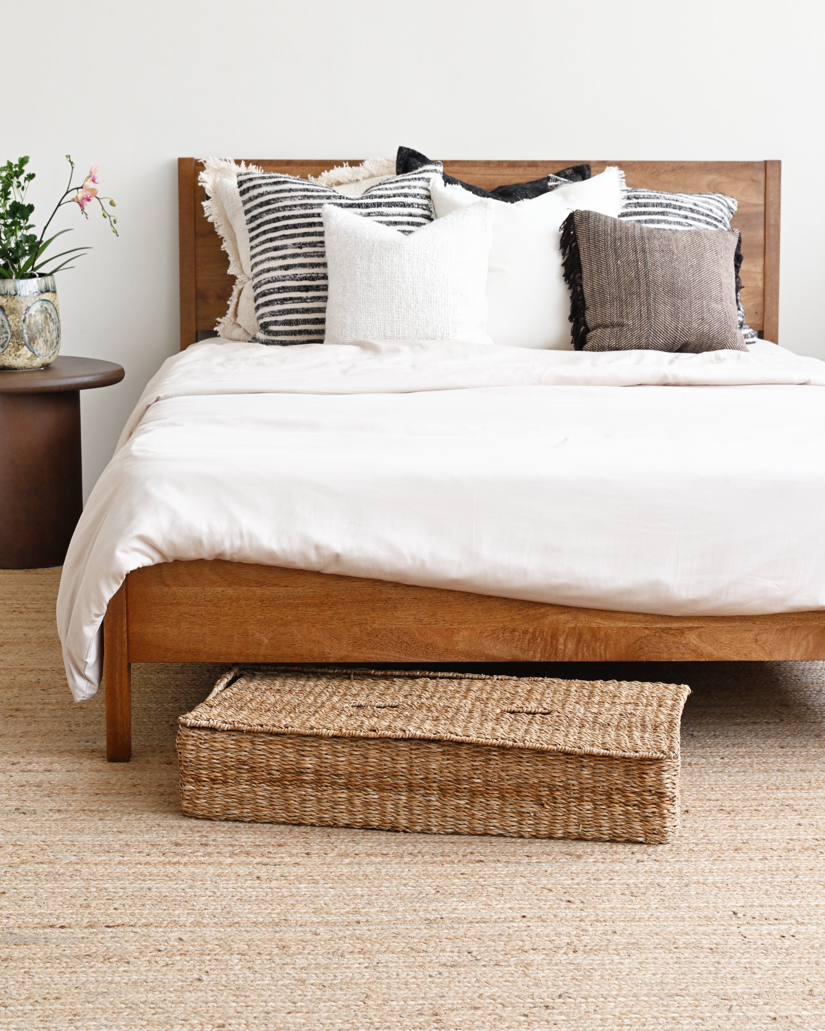Bedroom with wooden bed, white bedding, and a woven basket on a beige carpet.
