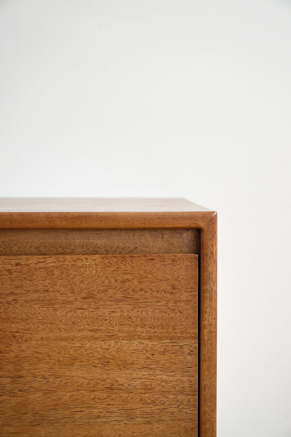 Close-up of a mid-century modern wooden chest or cabinet corner, showcasing a warm medium-brown wood grain finish against a plain white background.