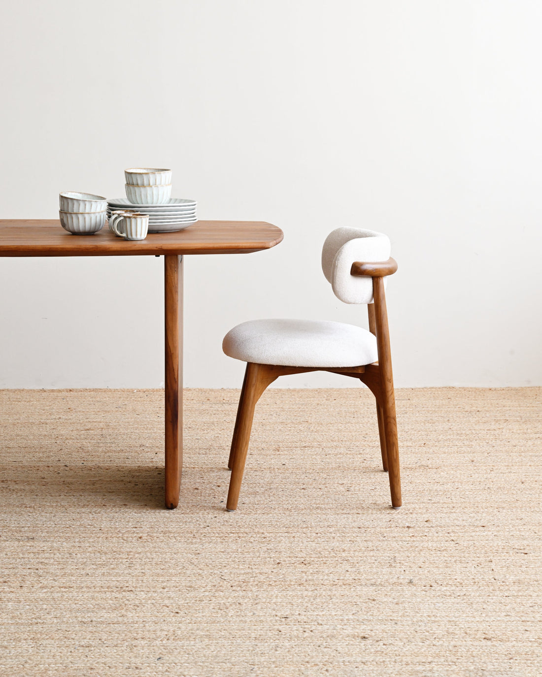 Wooden table with ceramic items and a white chair on a beige carpet.