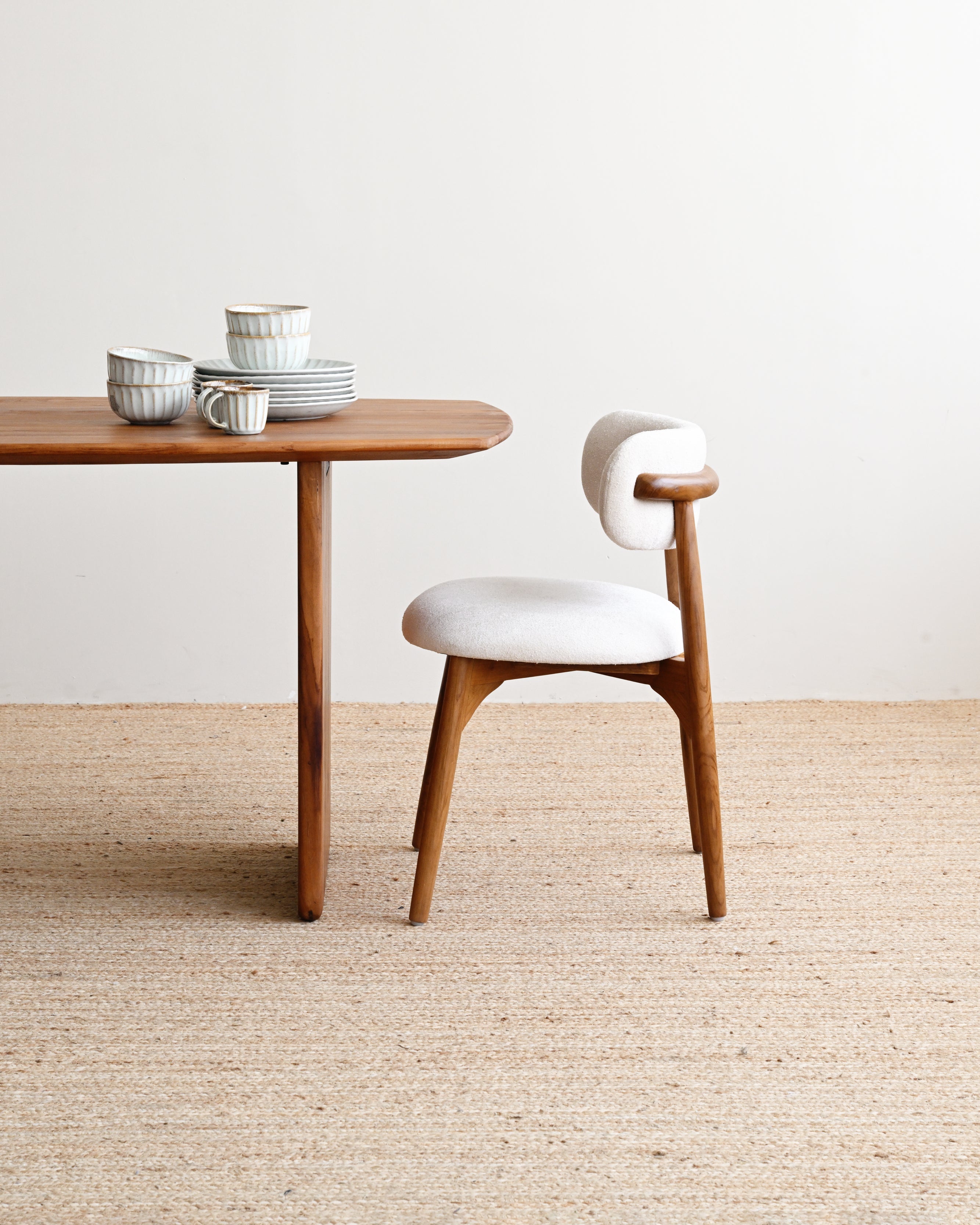 Wooden table with ceramic items and a white chair on a beige carpet.