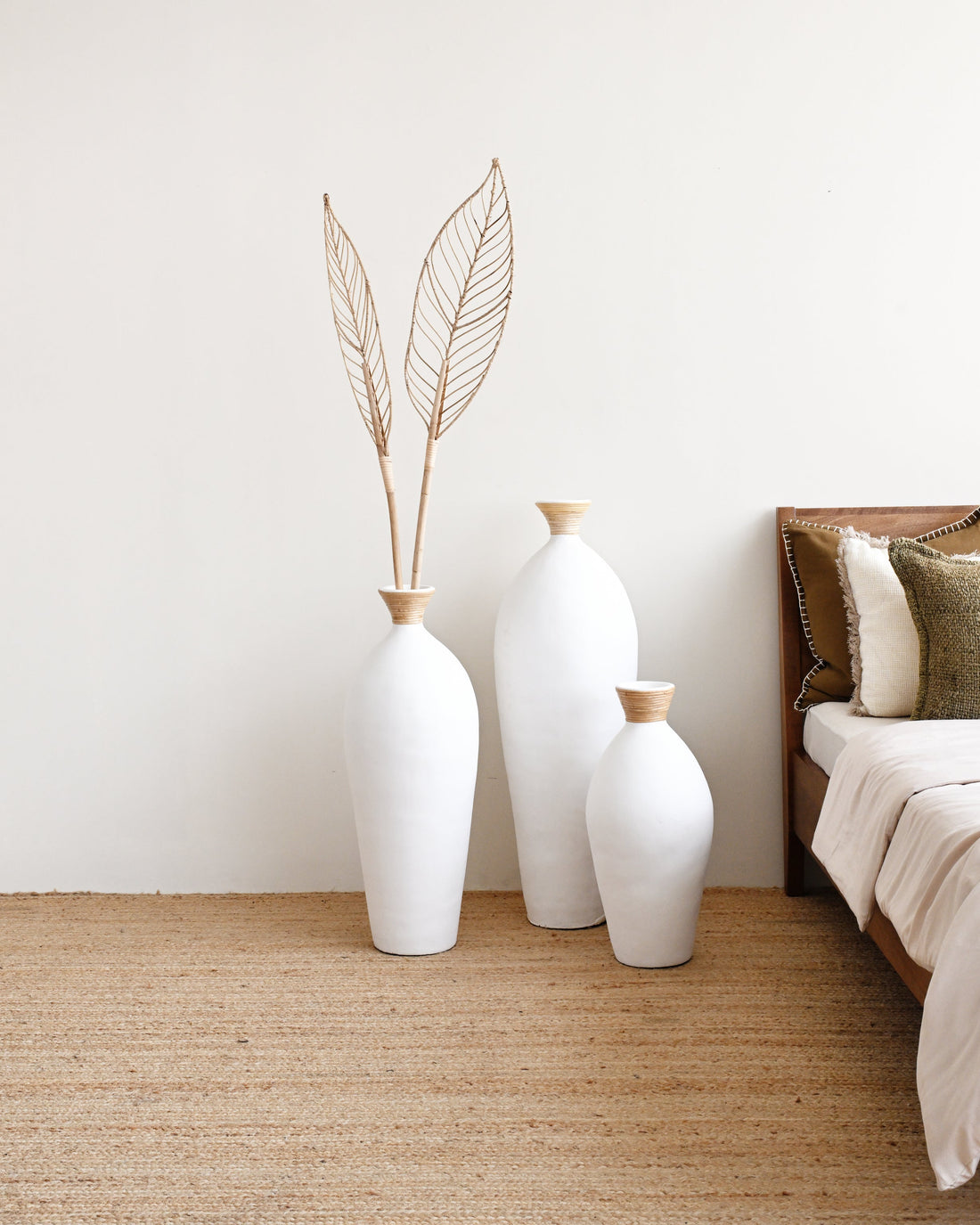 Three white vases with gold accents on a beige rug next to a bed.