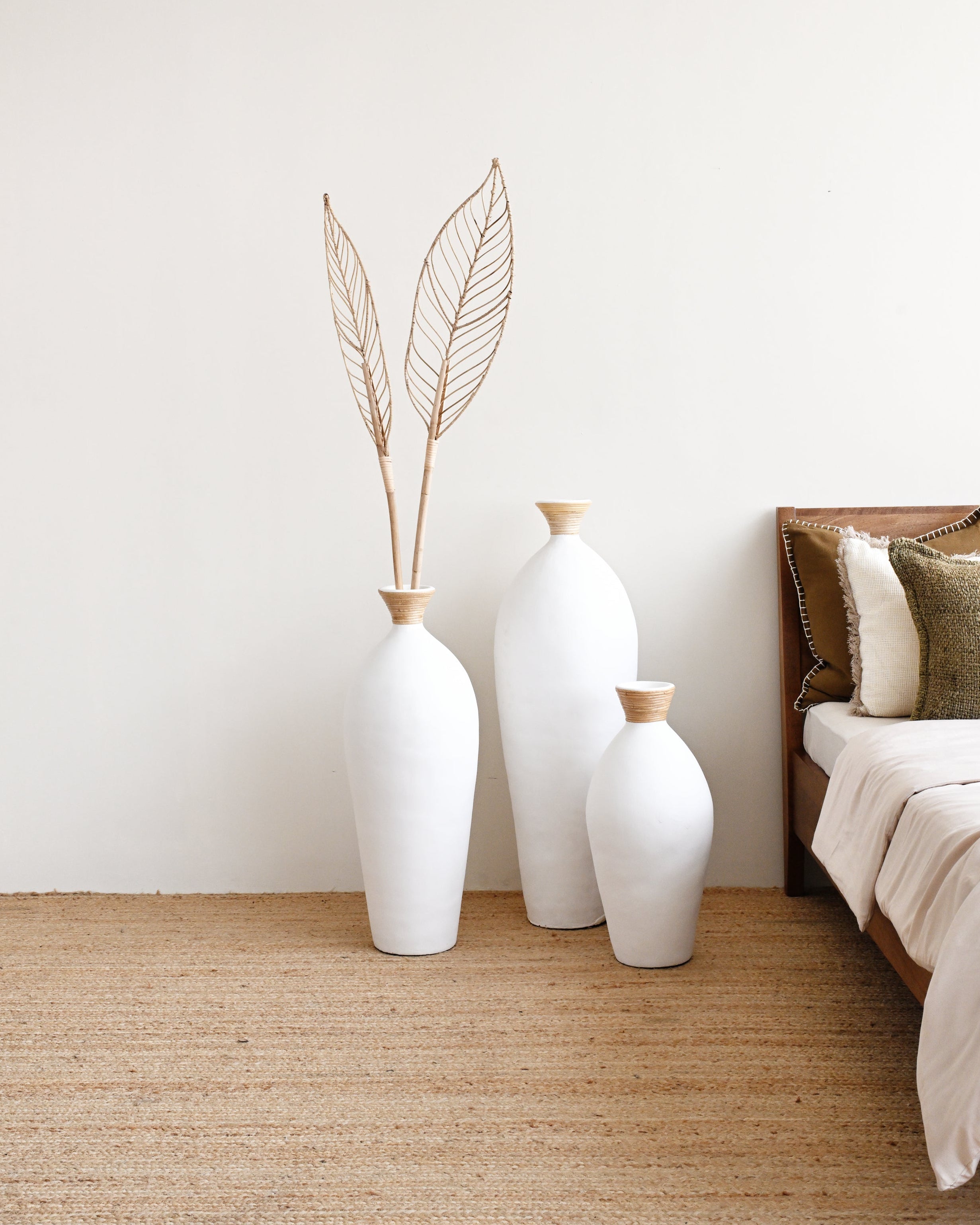 Three white vases with gold accents on a beige rug next to a bed.
