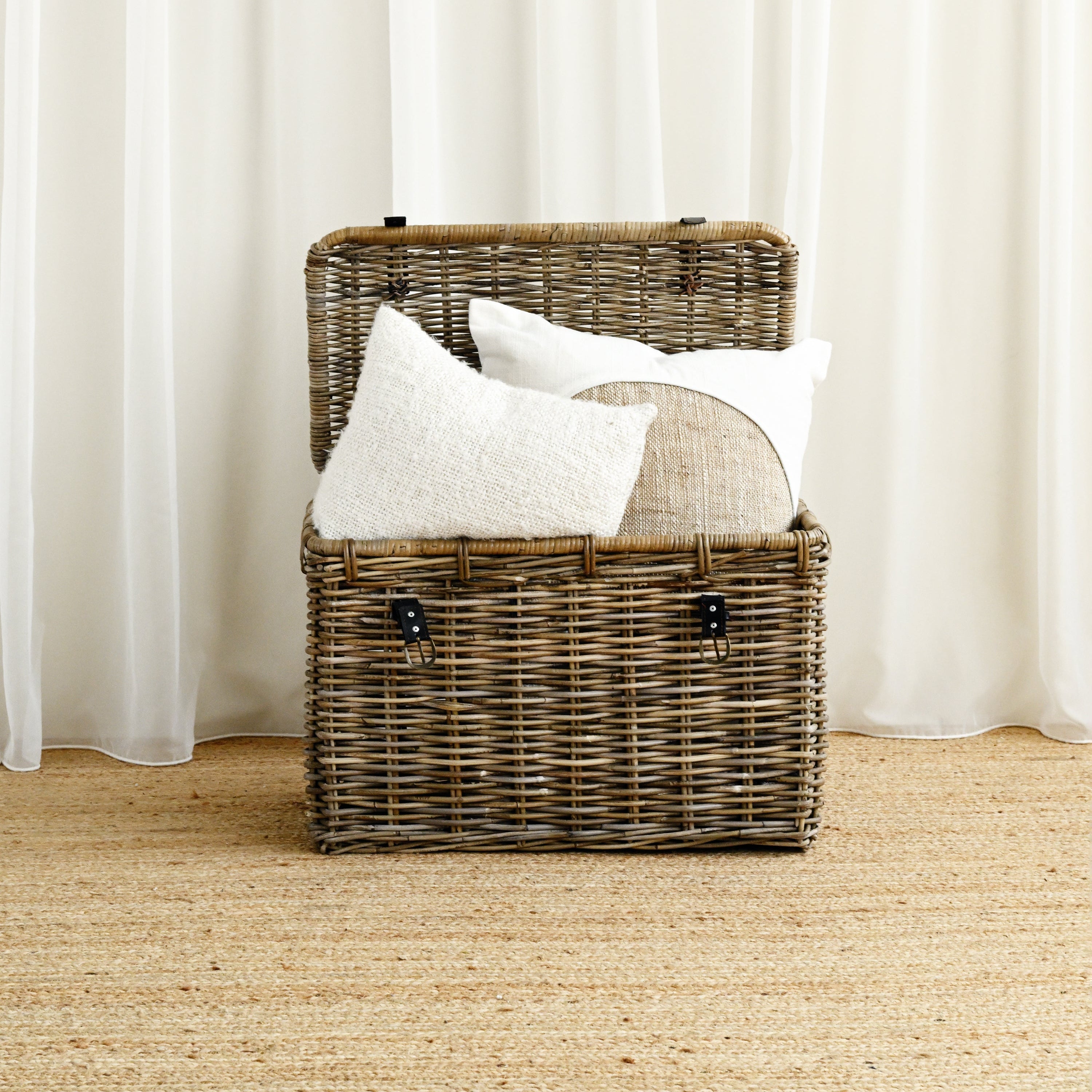 Wicker basket with white pillows against a white curtain background