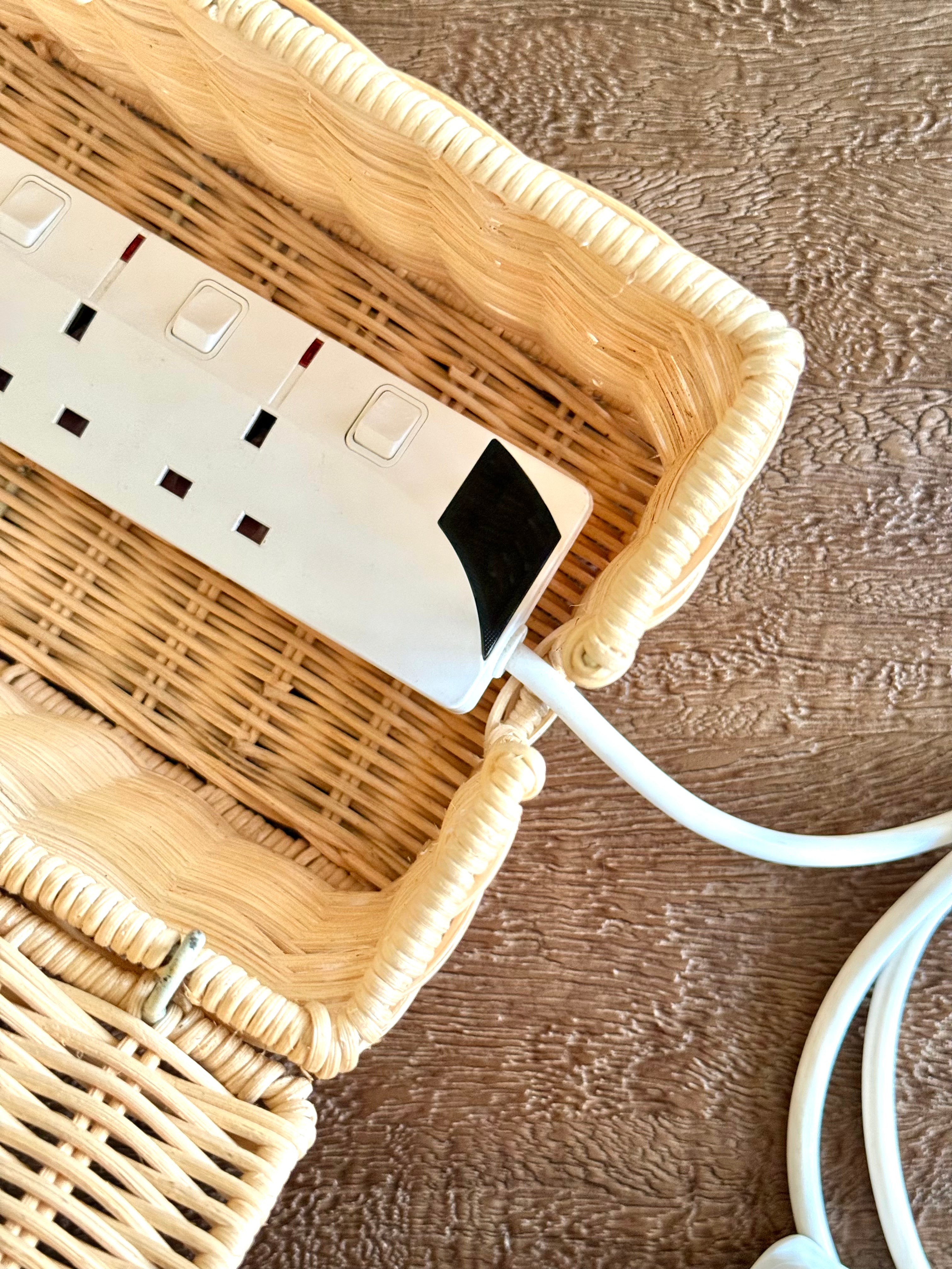 A white multi-outlet power strip with a black accent, resting inside a light beige woven wicker basket on a brown textured wooden surface.