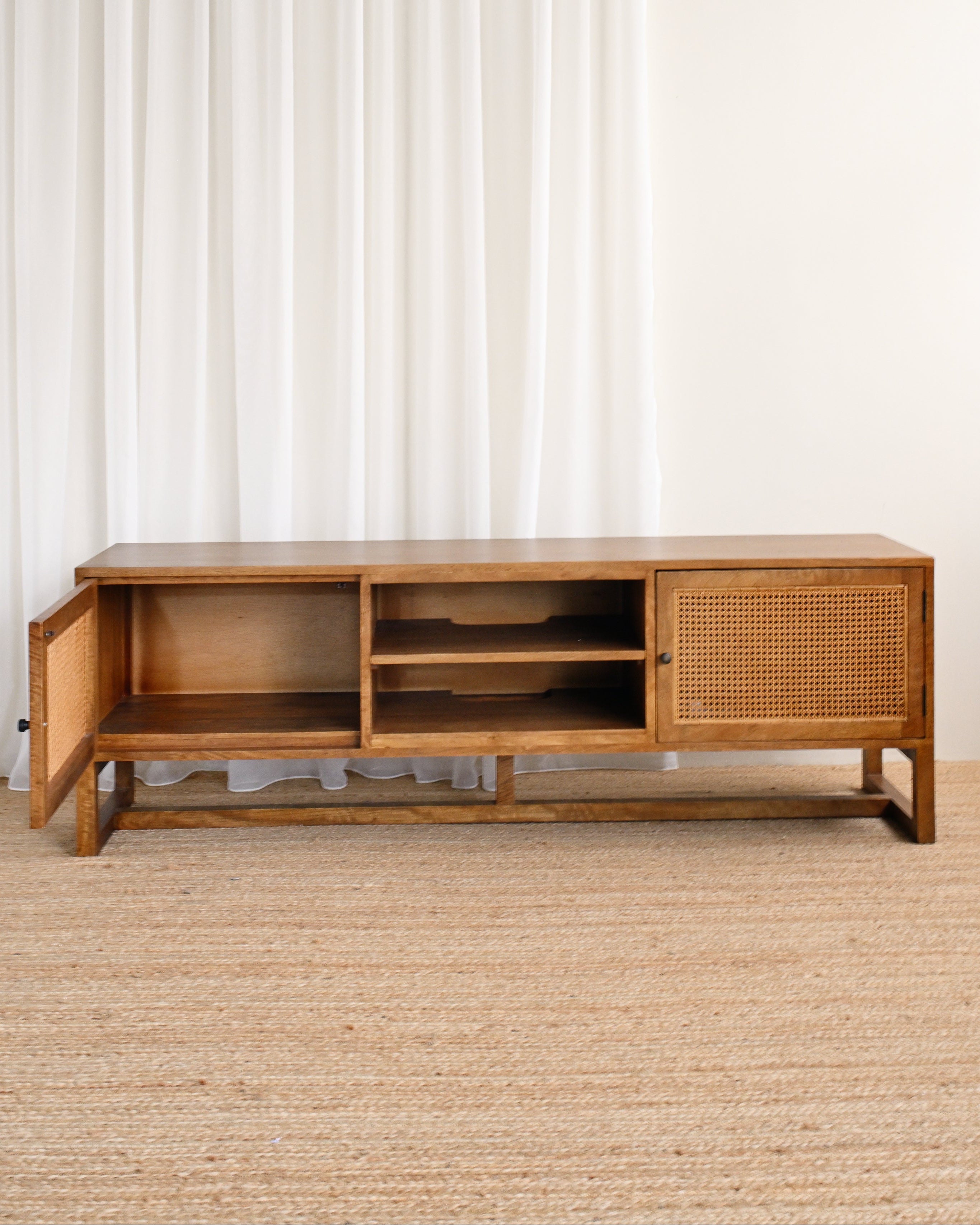 Wooden TV stand with wicker detailing against a white curtain background
