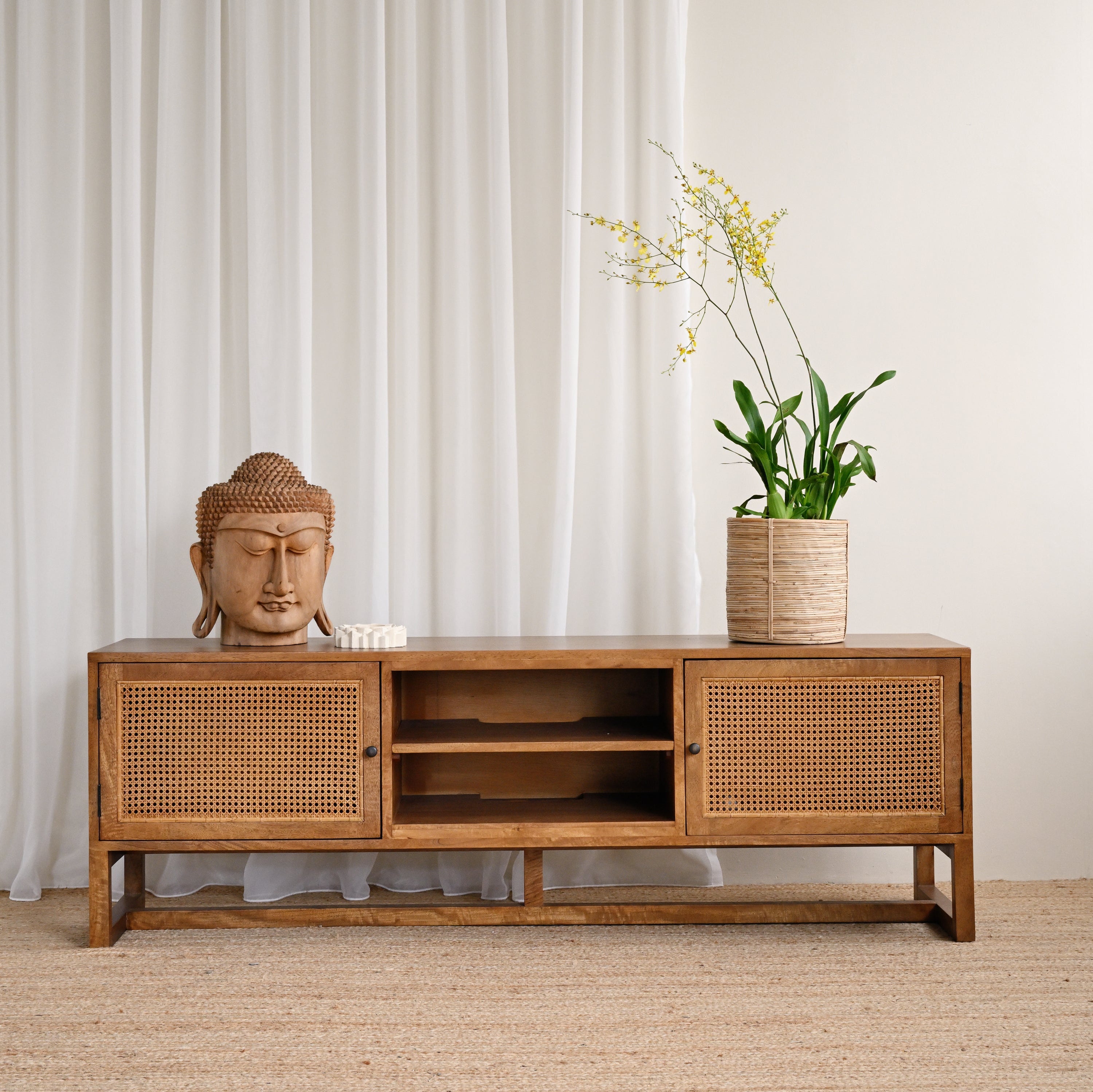 Wooden cabinet with a Buddha statue and potted plant against a white curtain background
