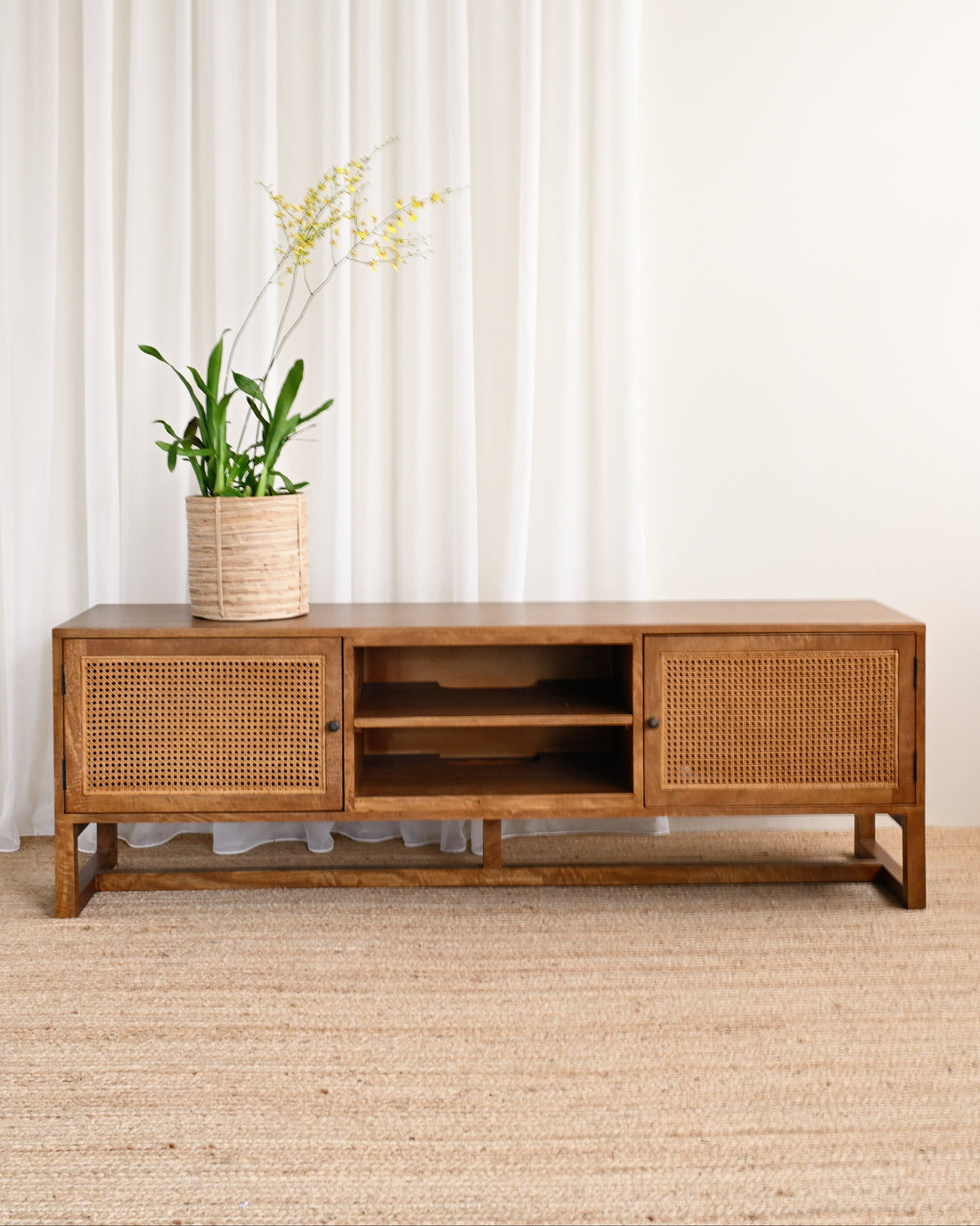 Wooden TV stand with wicker doors against a white curtain background
