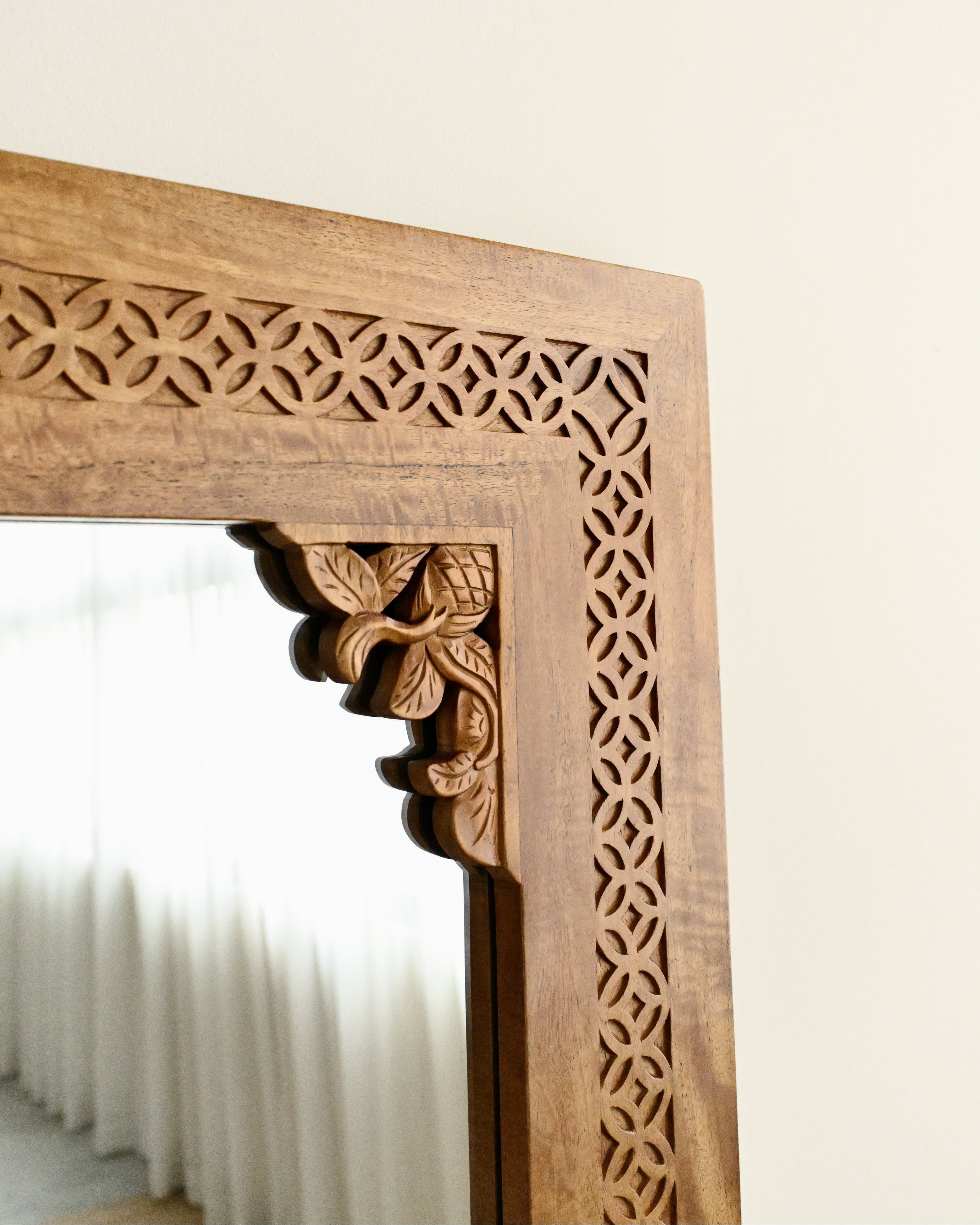 Close-up of a wooden mirror frame with intricate carvings on a white background