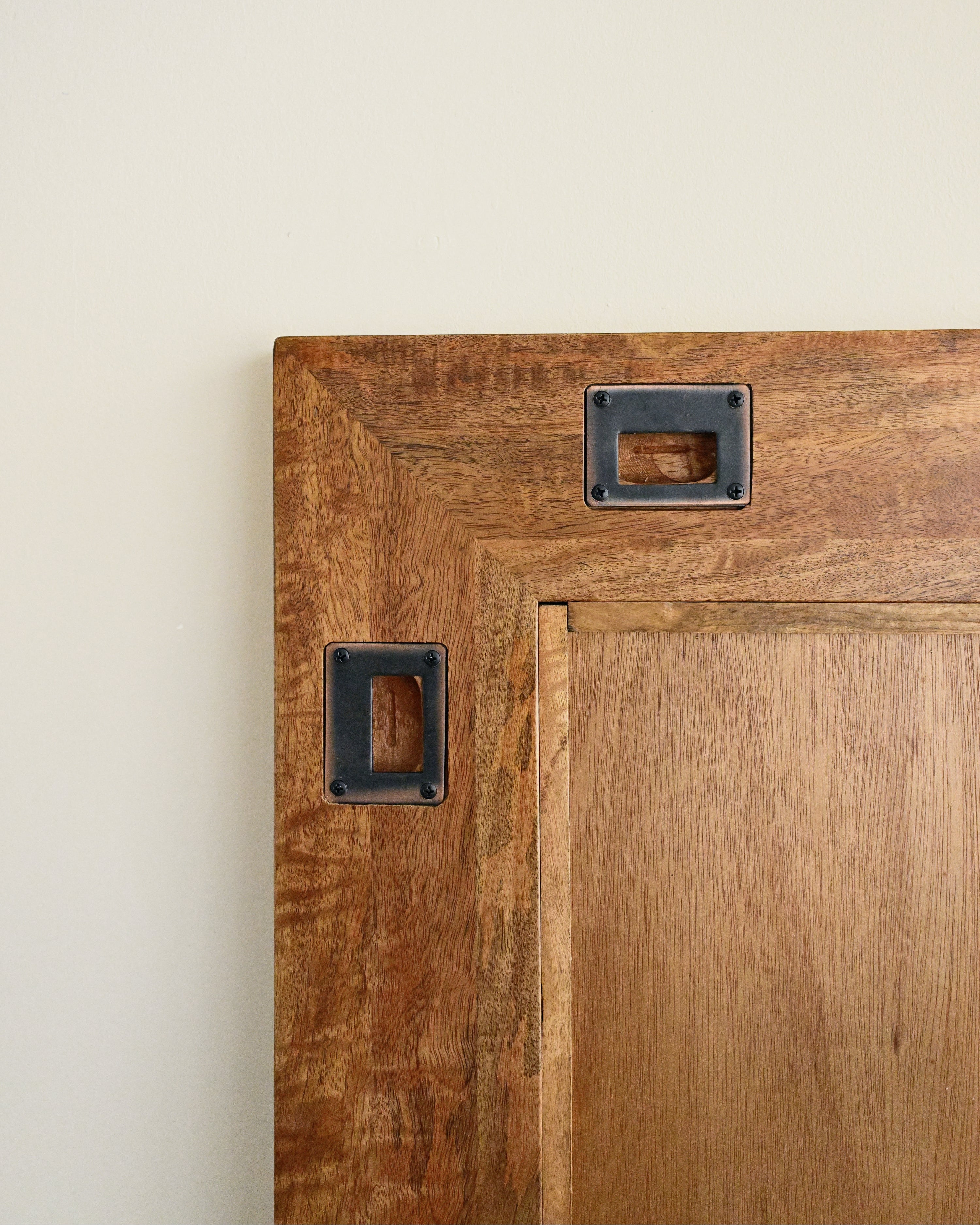 Close-up of a wooden cabinet with metal handles on a beige wall.