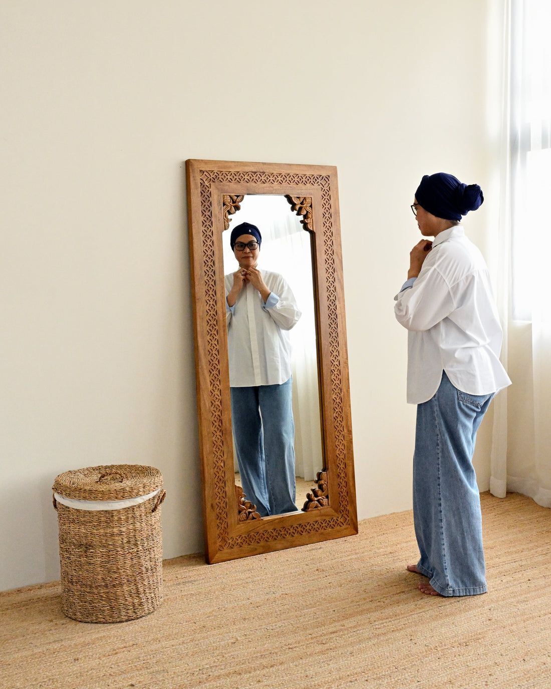 Person standing in front of a large solid wood standing mirror in a room with a woven basket on the floor.