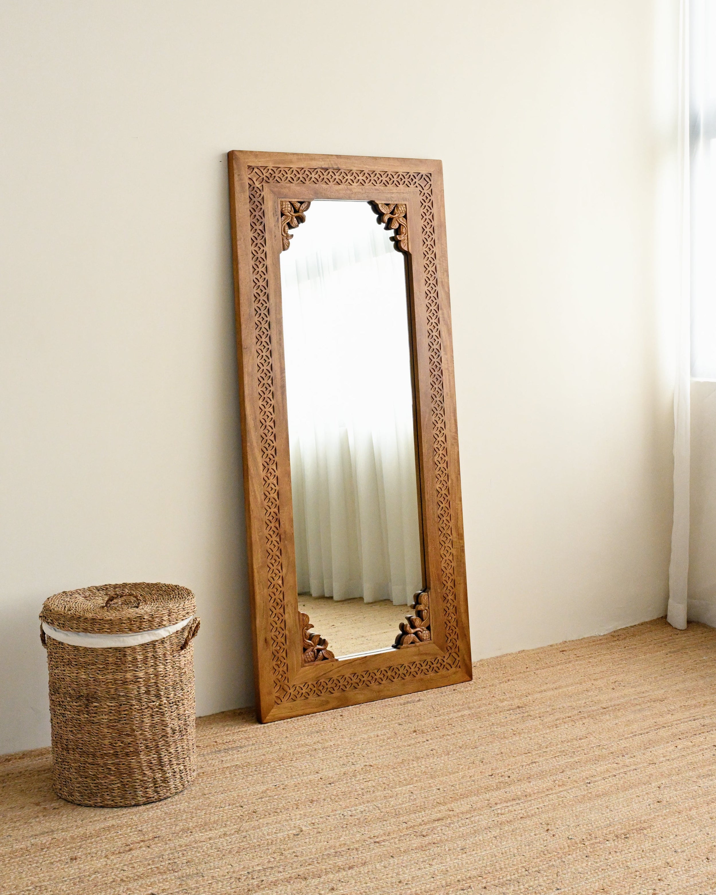 solid mango wood mirror with intricate hand carved detailing, next to a laundry basket