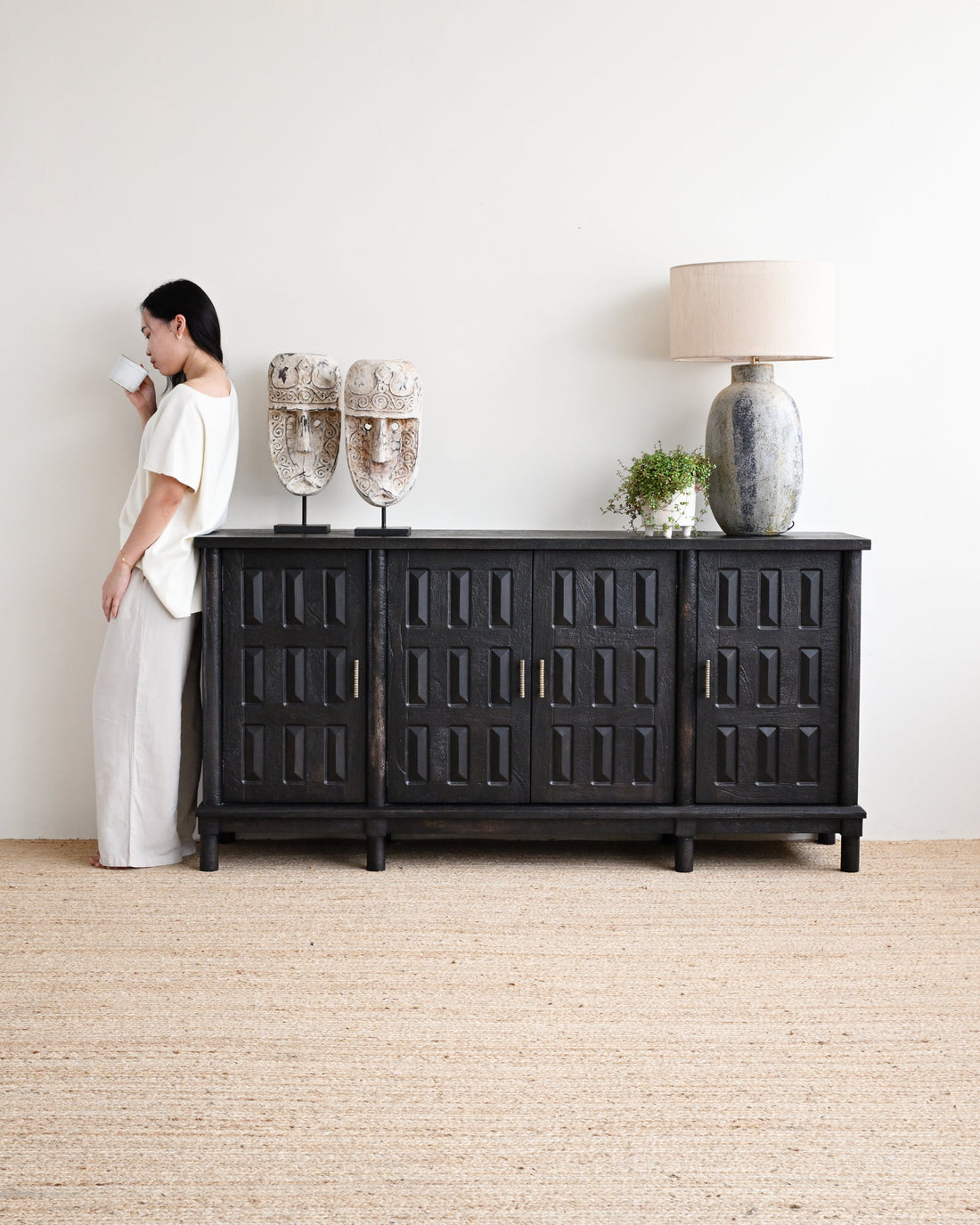 Woman standing next to a black sideboard with decorative items in a minimalistic room.