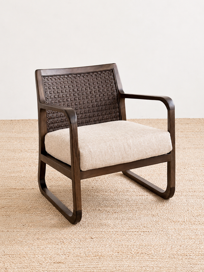 Brown wicker armchair with beige cushion on a light wooden floor.