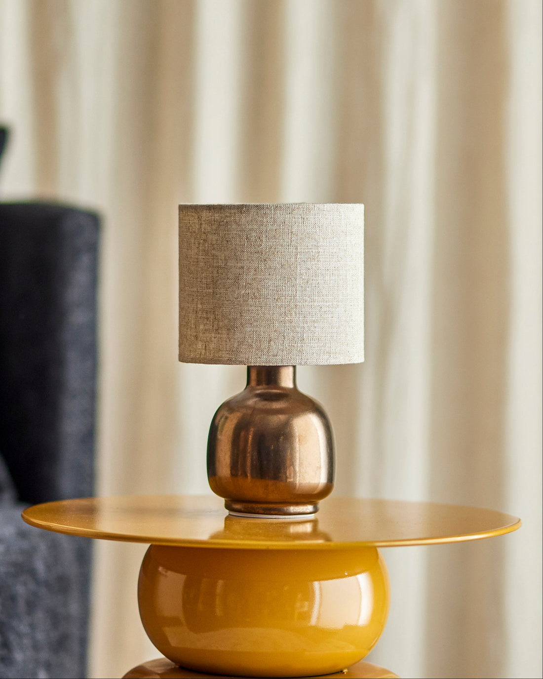Yellow side table with a bronze lamp featuring a textured gray shade.