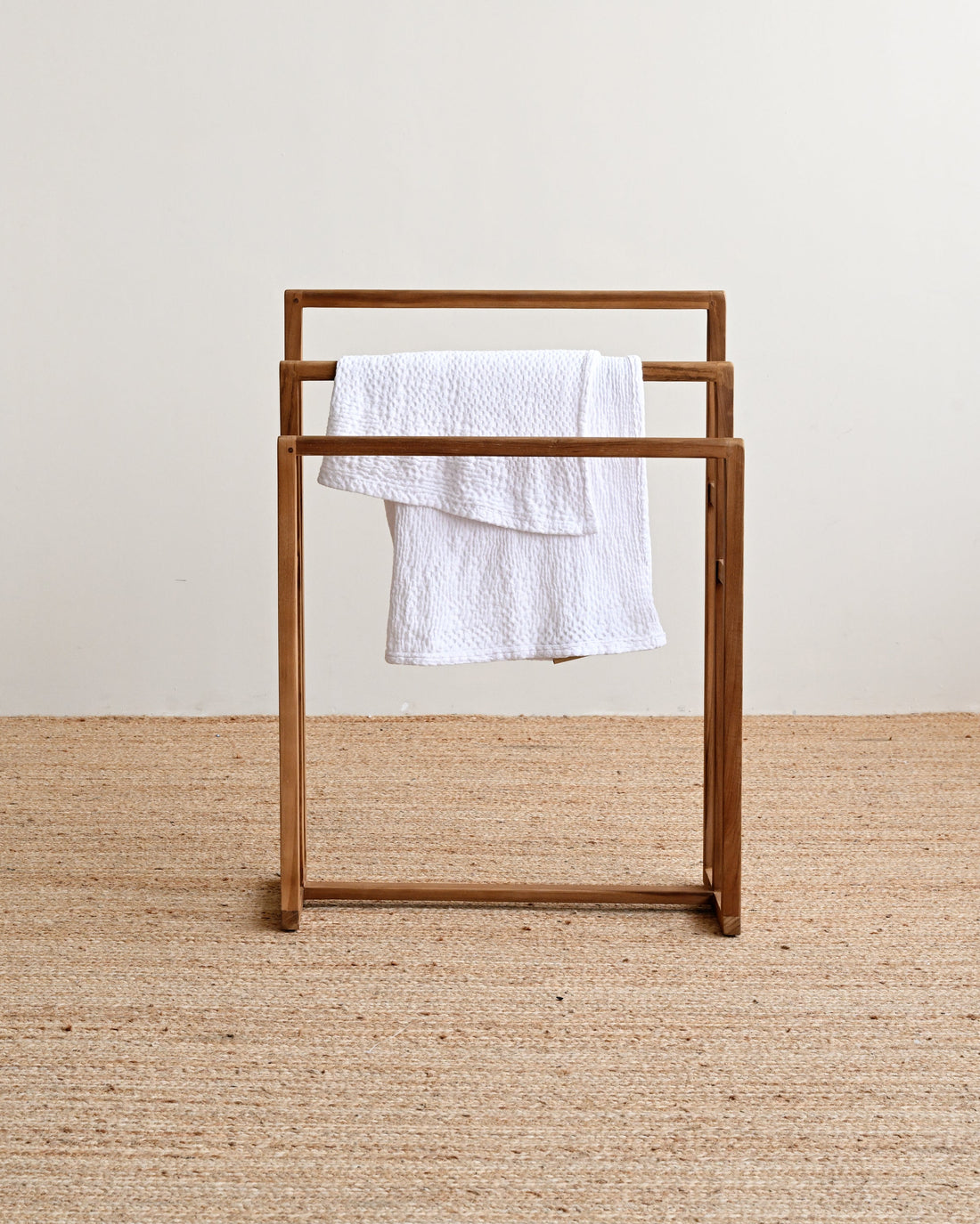 Wooden towel rack with a white towel on a beige carpet and light-colored wall background
