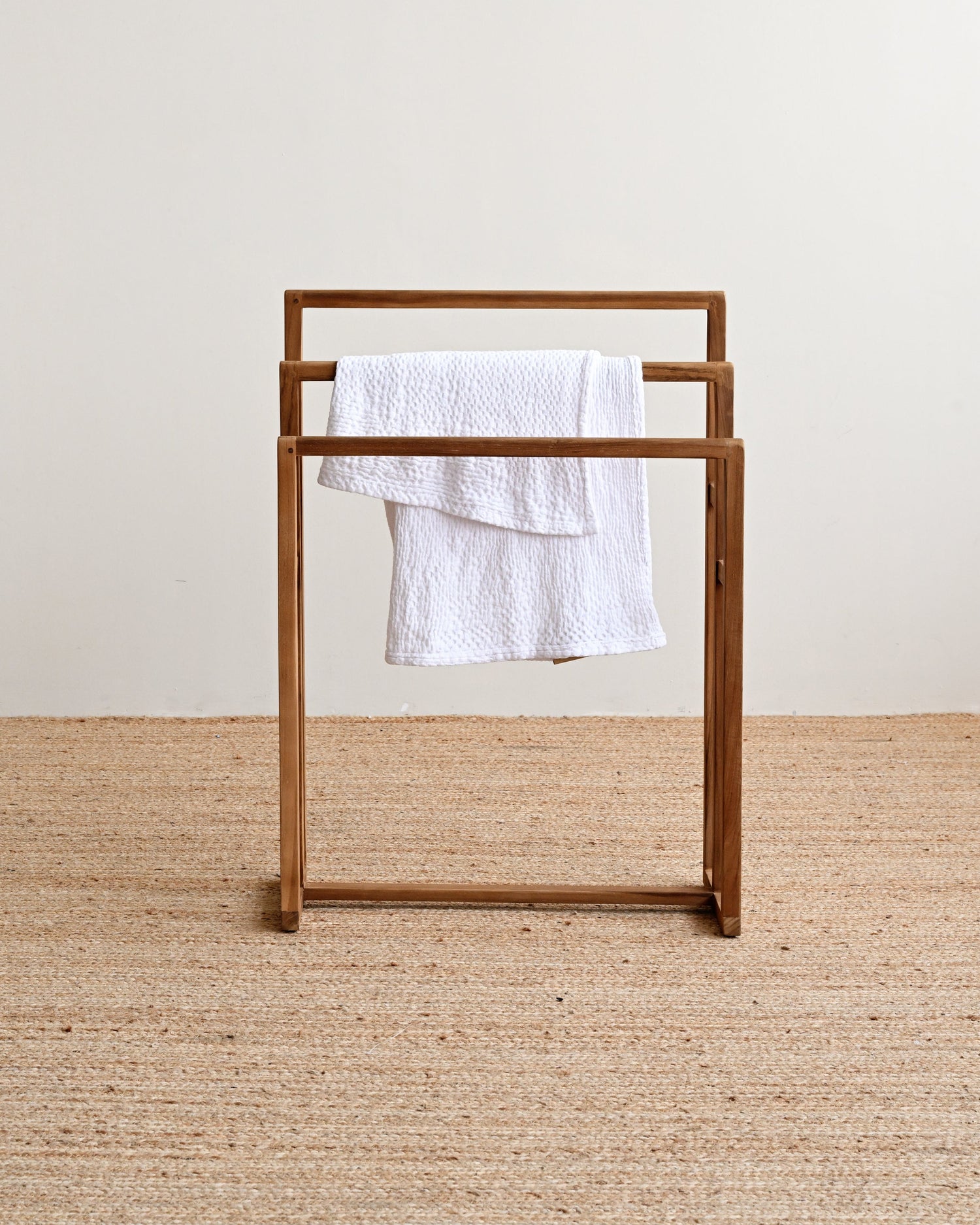 Wooden towel rack with a white towel on a beige carpet and light-colored wall background