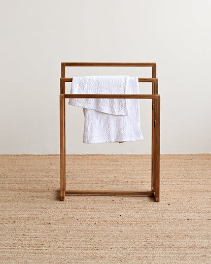 Wooden towel rack with a white towel on a beige carpet and light-colored wall background