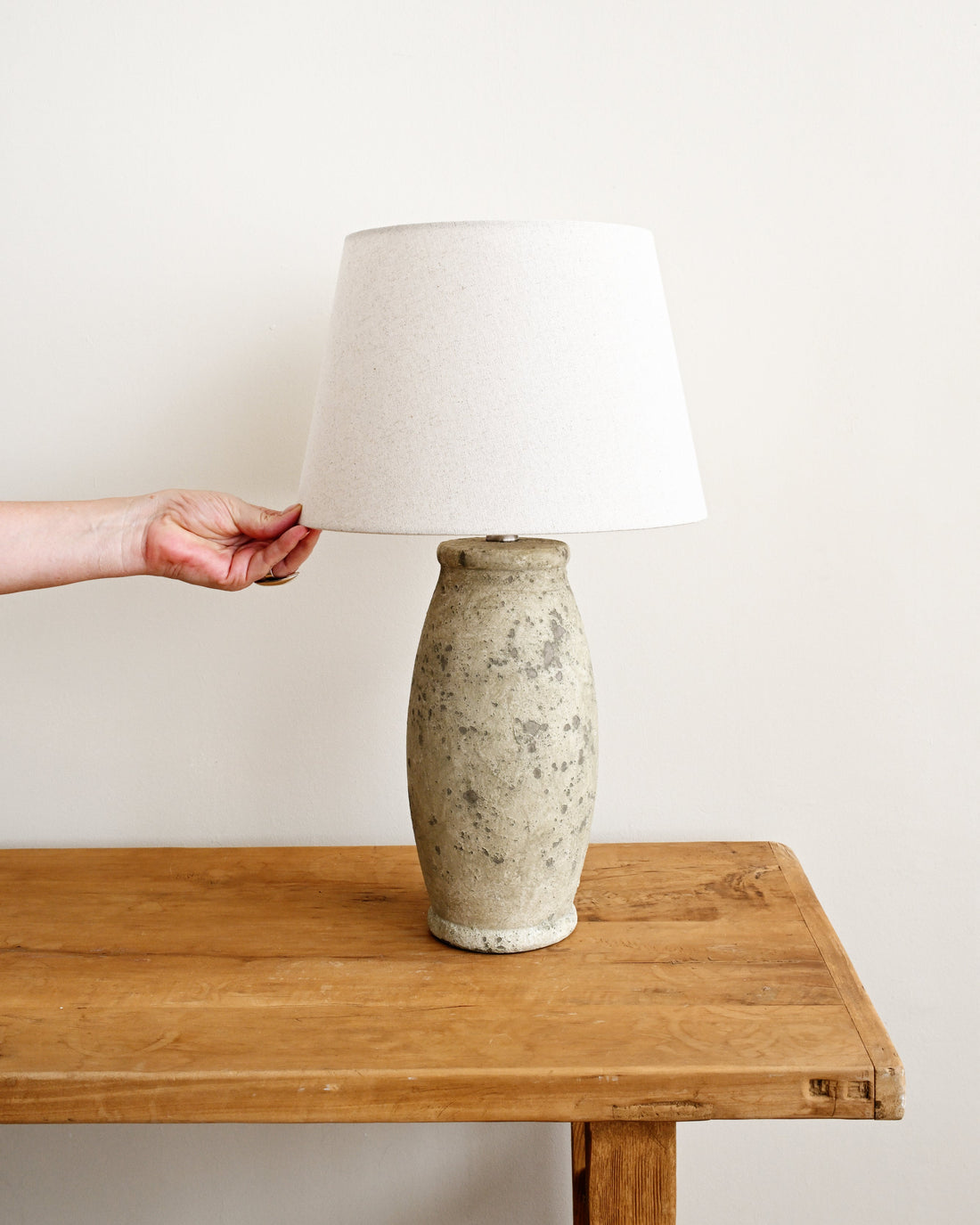 Person adjusting a lamp on a wooden table with a plain background