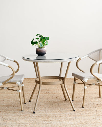 Round glass table with a plant and two chairs on a beige carpet