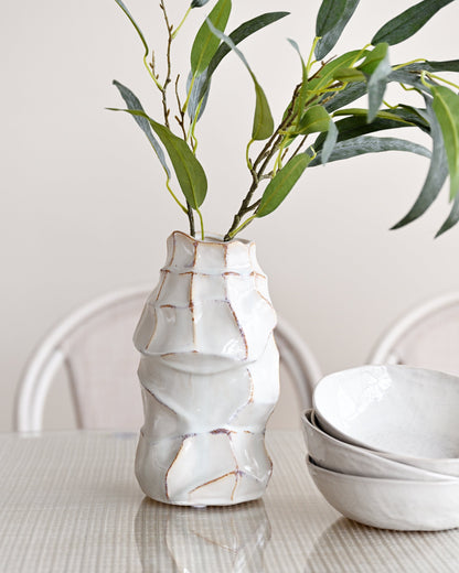 White ceramic vase with wavy texture holding green leaves on a light surface.