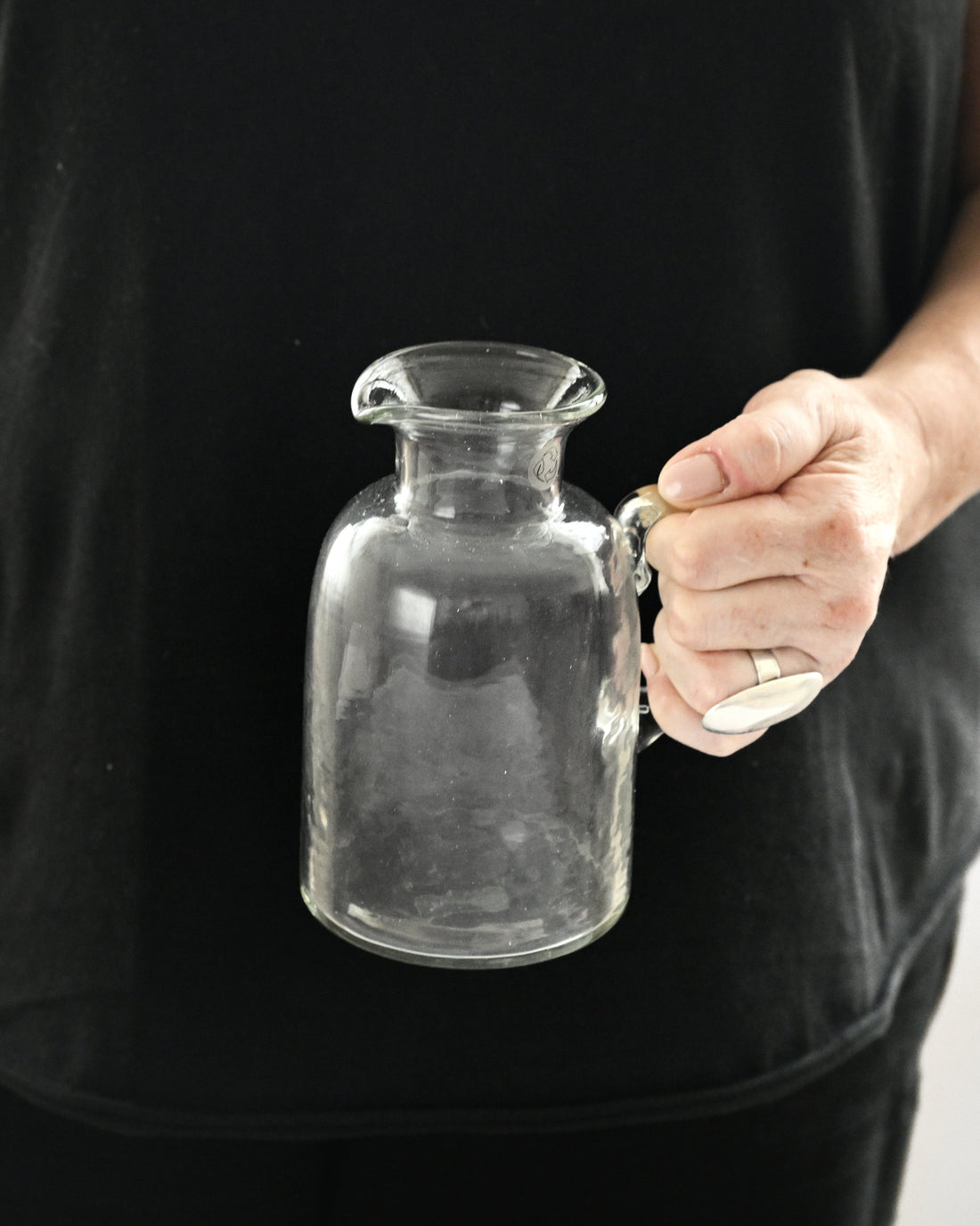Person holding a clear glass bottle against a black background