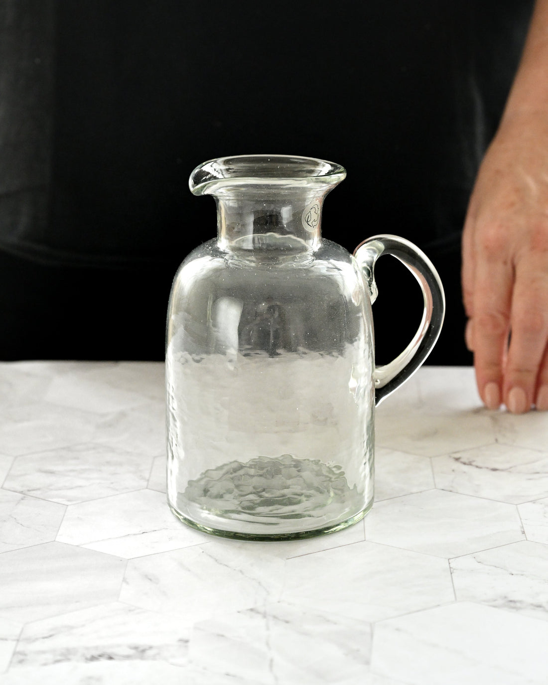 Clear glass pitcher on a white surface with a blurred background