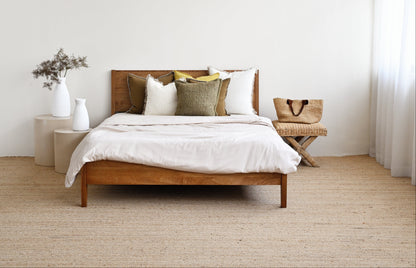 Wooden bed with white bedding and pillows in a minimalistic bedroom.