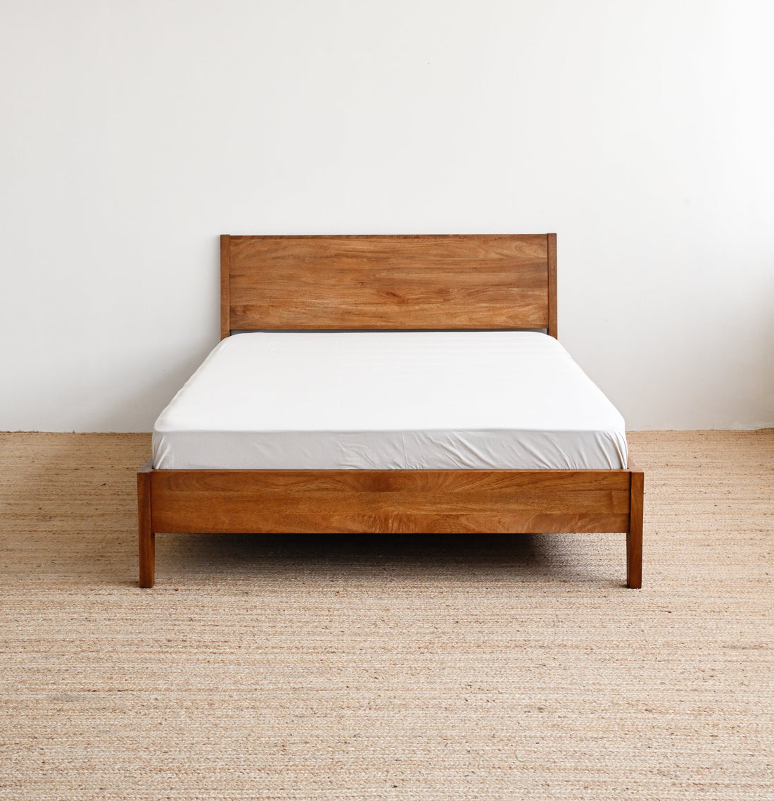 Wooden bed with white mattress against a plain wall