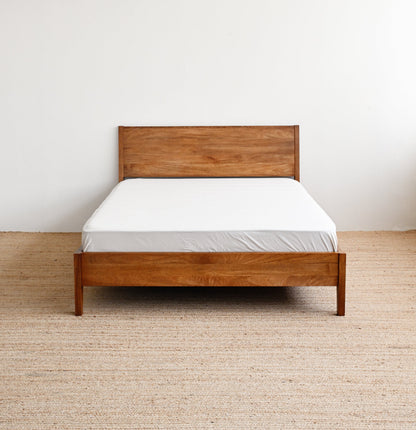 Wooden bed with white mattress against a plain wall