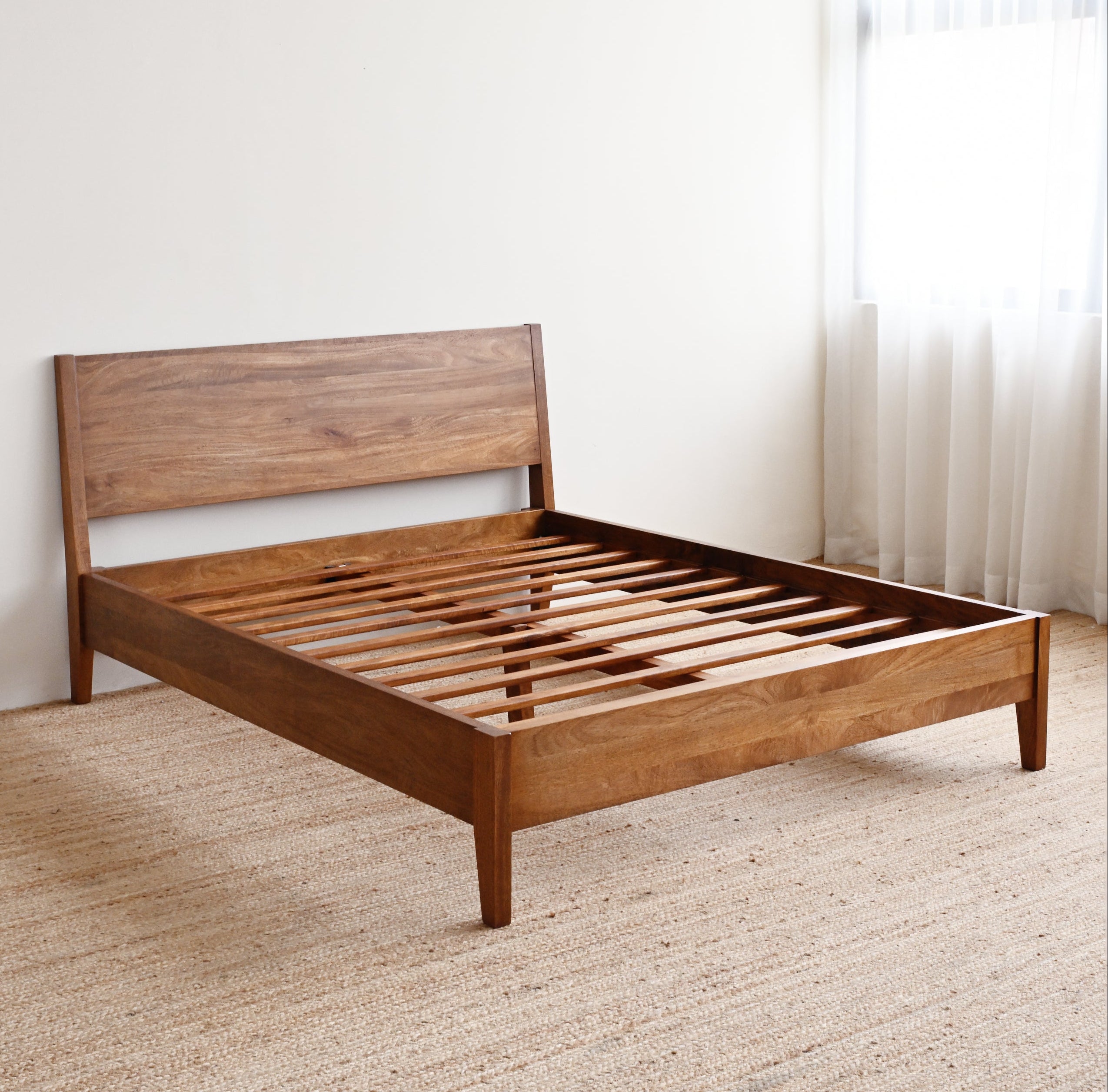 Wooden bed frame in a room with a carpeted floor and a window.
