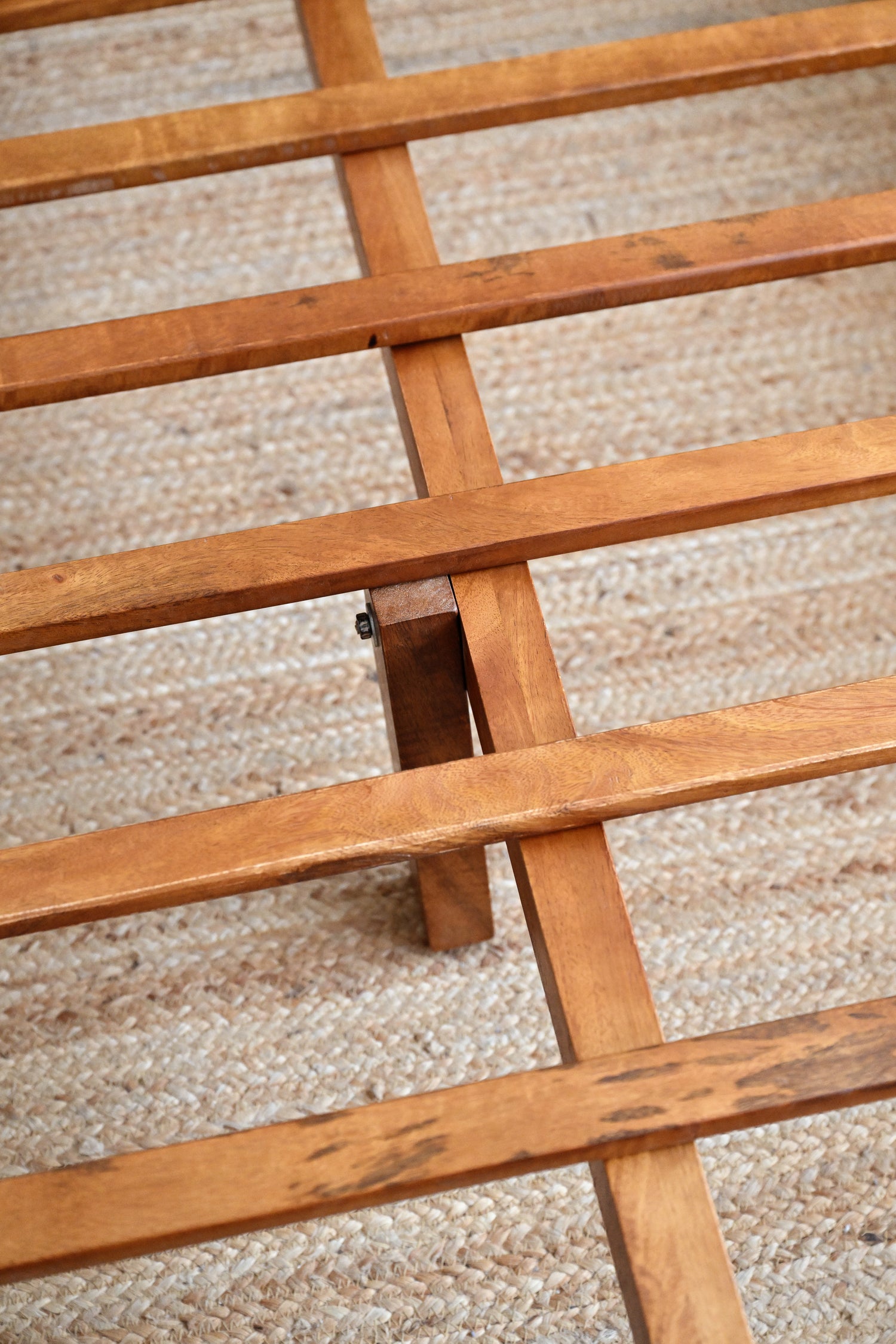 Close-up of a wooden slatted bed frame on a carpeted floor.