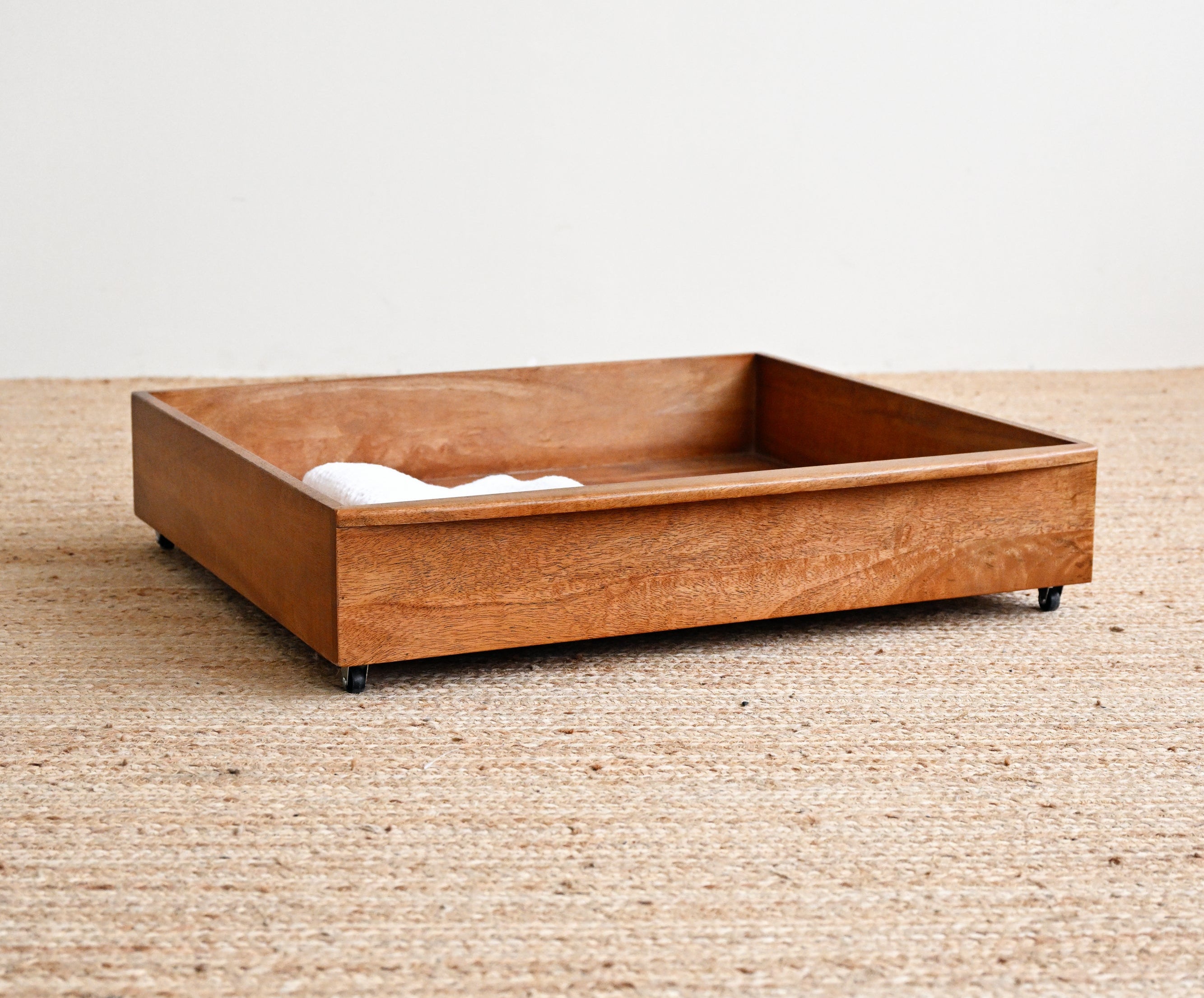 Wooden pet bed on a textured beige floor with a white wall background