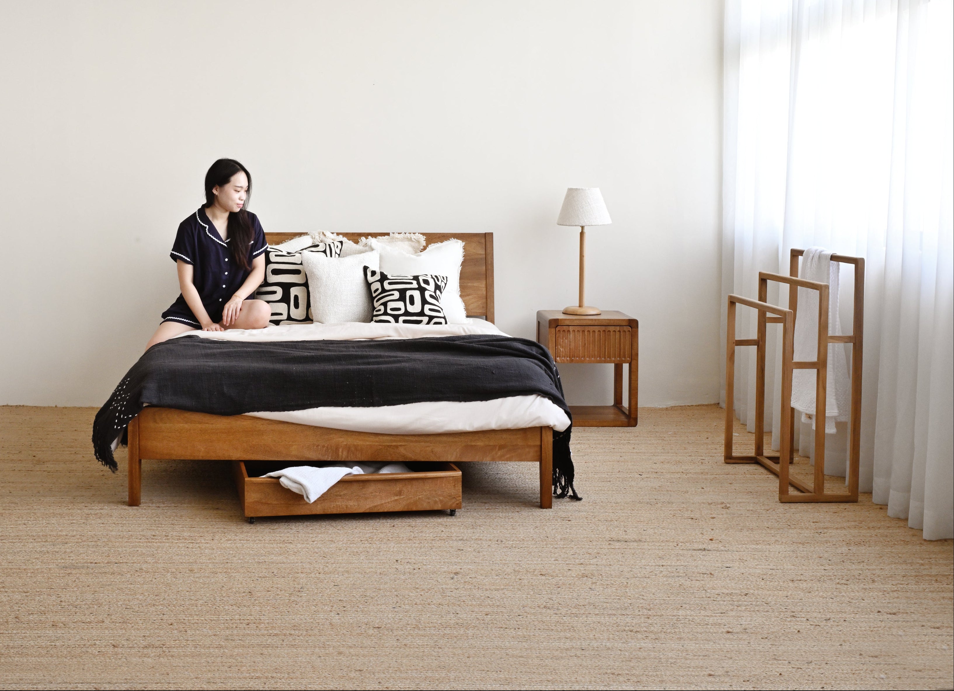 Woman sitting on a bed in a minimalistic bedroom with wooden furniture.