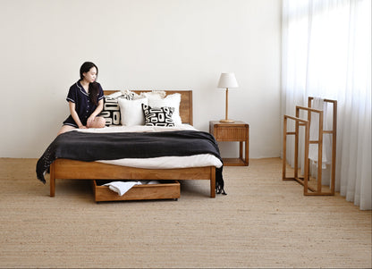 Woman sitting on a bed in a minimalistic bedroom with wooden furniture.