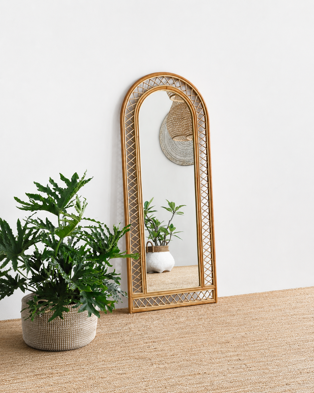 Rattan-framed mirror on a wooden surface with a plant next to it