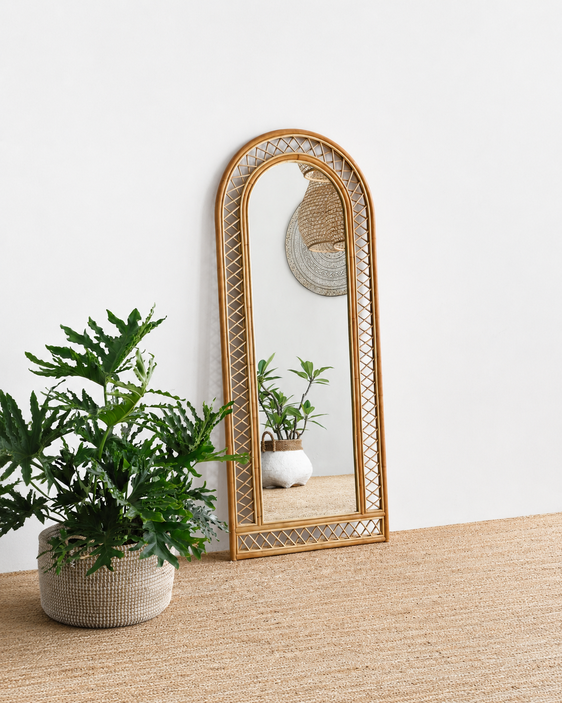 Rattan-framed mirror on a wooden surface with a plant next to it