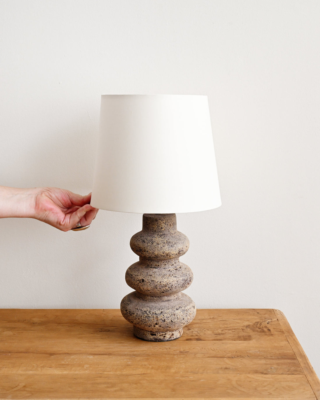 Person adjusting a lamp with a textured base and white shade on a wooden surface.