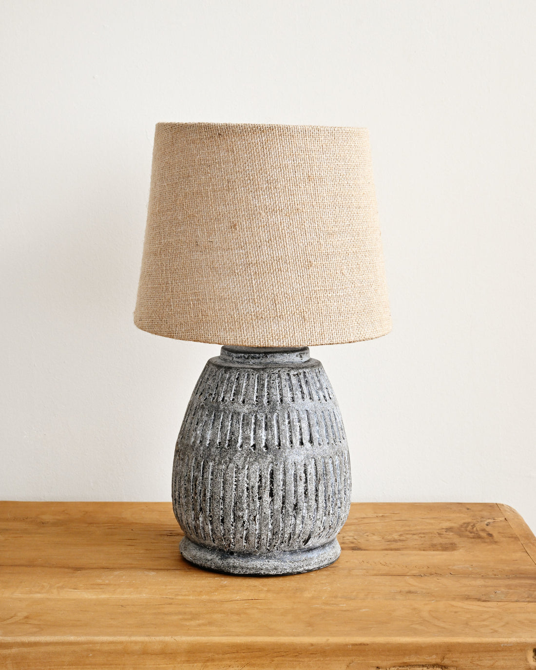 Table lamp with textured base and beige lampshade on a wooden surface.