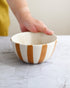 Hand holding a ceramic bowl with brown and white stripes on a marble surface.