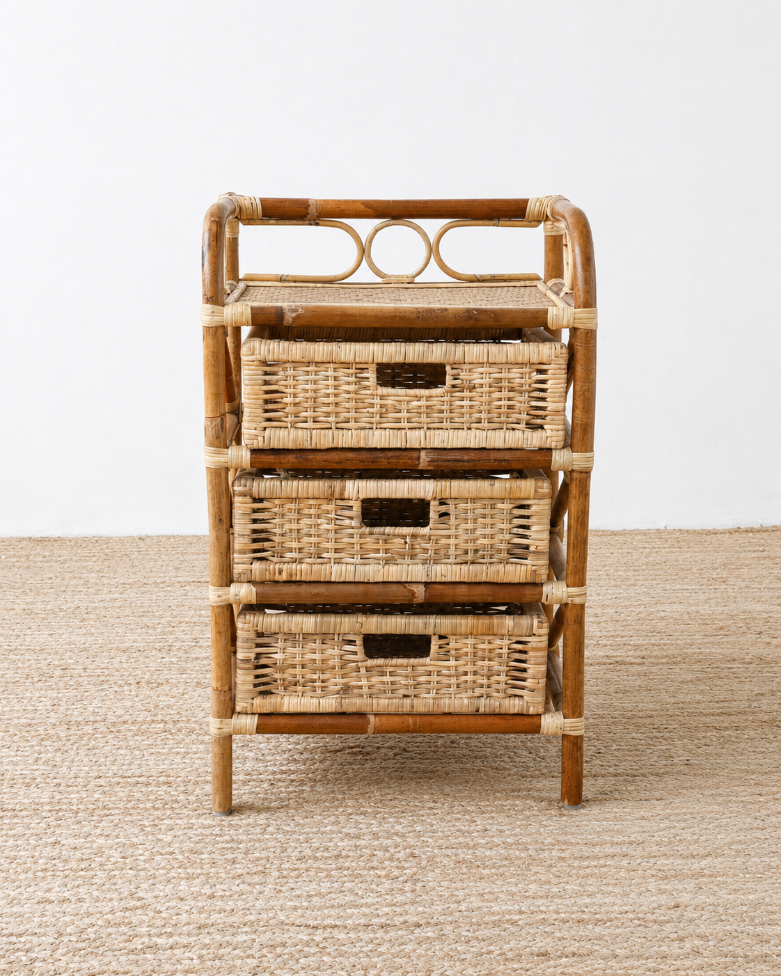 Rattan cabinet with three woven drawers on a neutral background