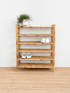 Bamboo shoe rack with shoes and a plant on a wooden floor against a white wall.