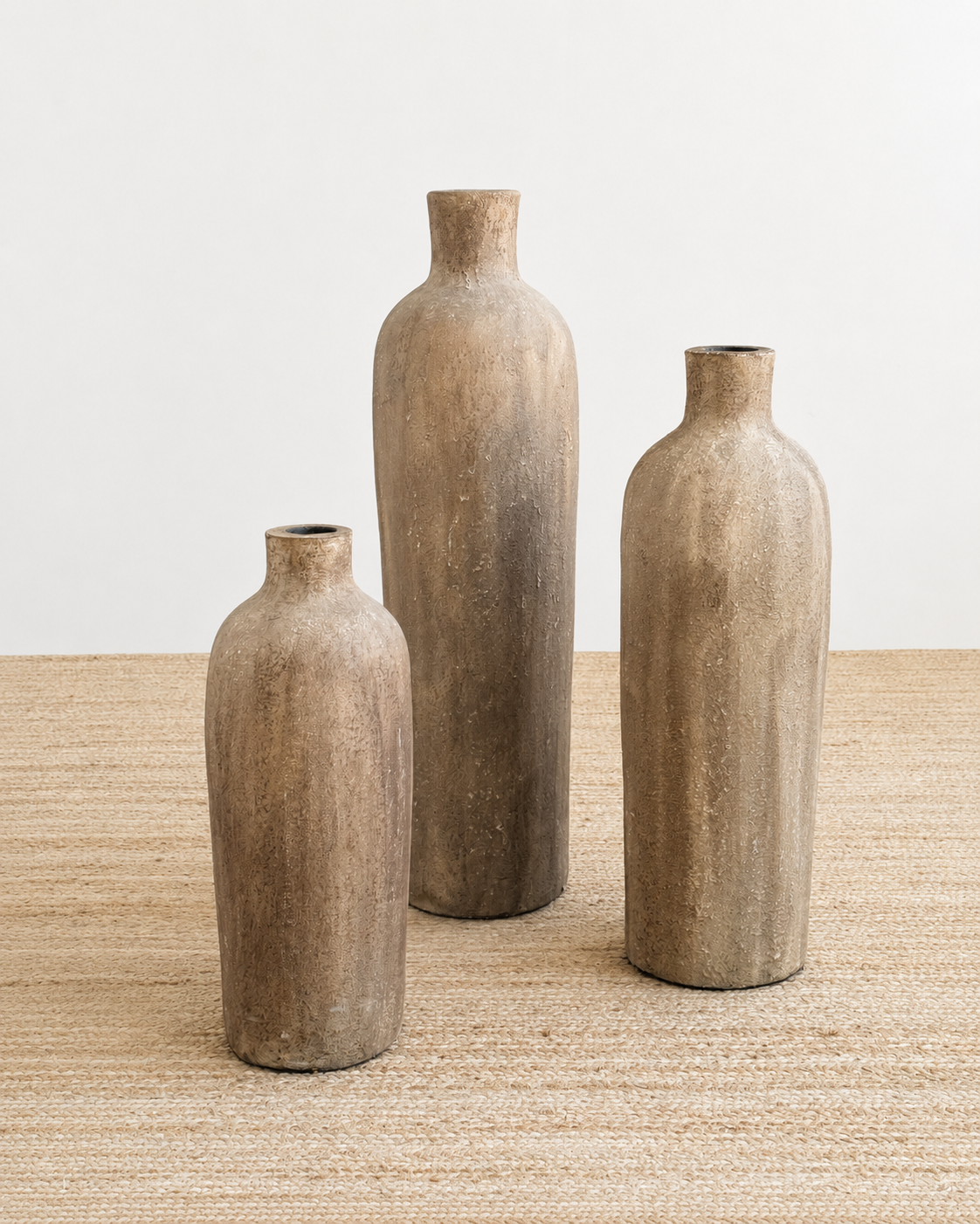 Three rustic-style vases of different sizes on a textured surface with a neutral background