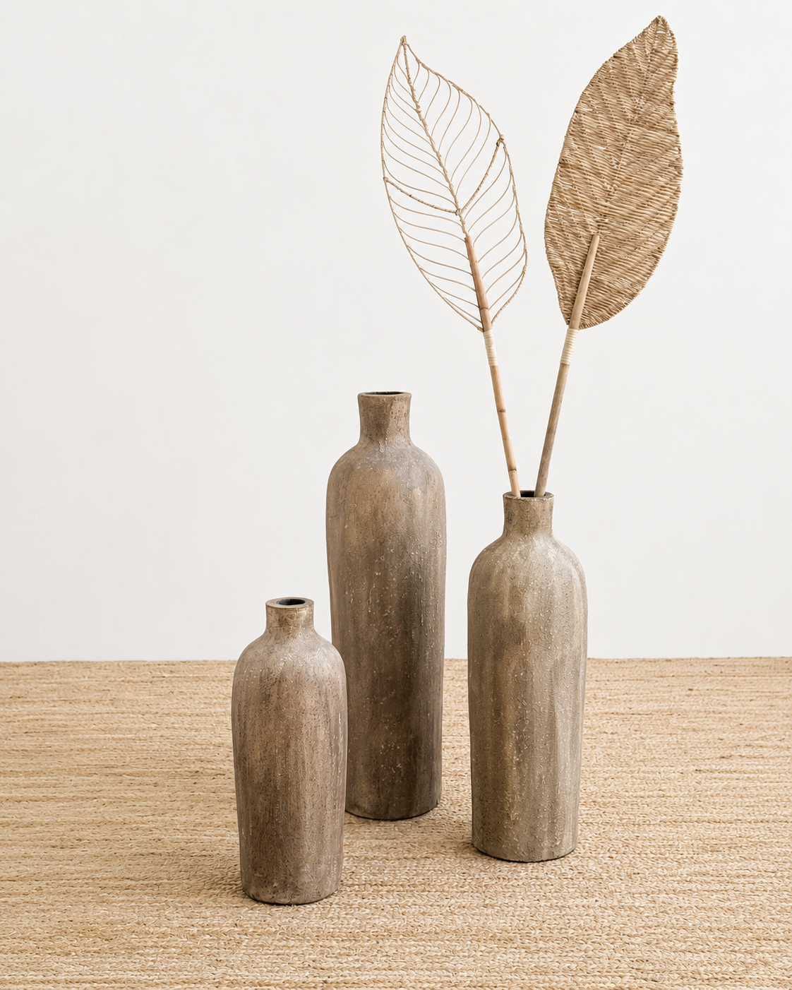 Three rustic vases on a textured surface with decorative leaves.