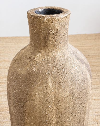 Textured brown vase on a woven surface with a neutral background