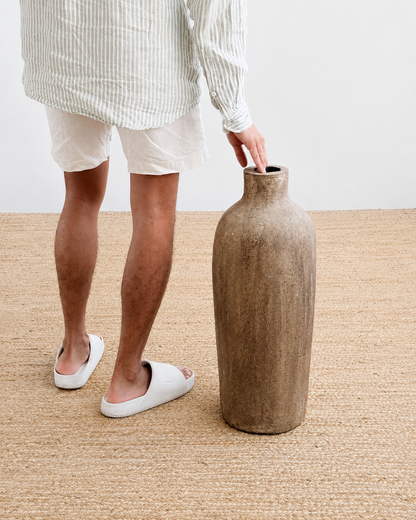 Person holding a large brown vase on a beige carpet