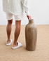 Person holding a large brown vase on a beige carpet